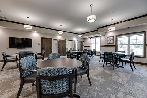 Spacious community room with tables and chairs, carpeted floor, and large windows.