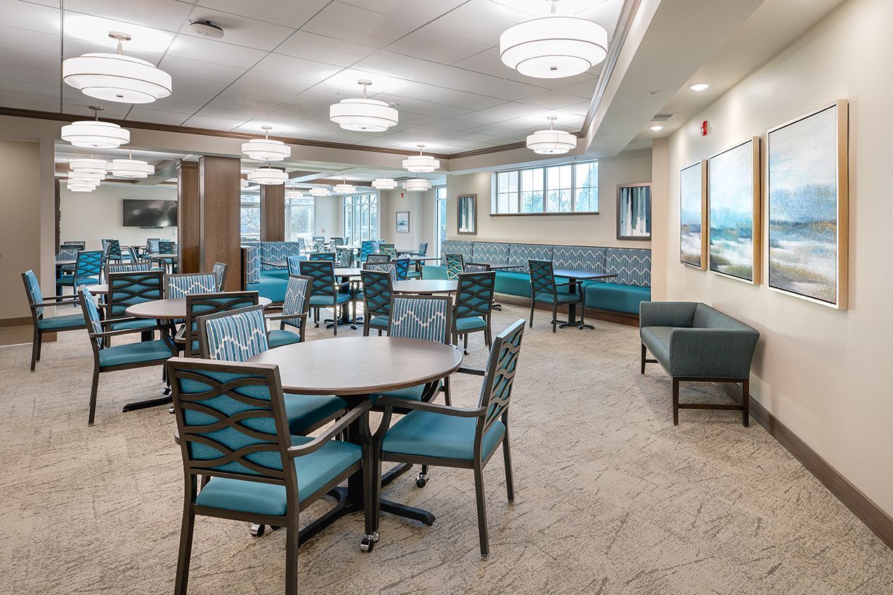 A dining area with round tables, teal chairs, and recessed lighting. Artwork hangs on the wall.