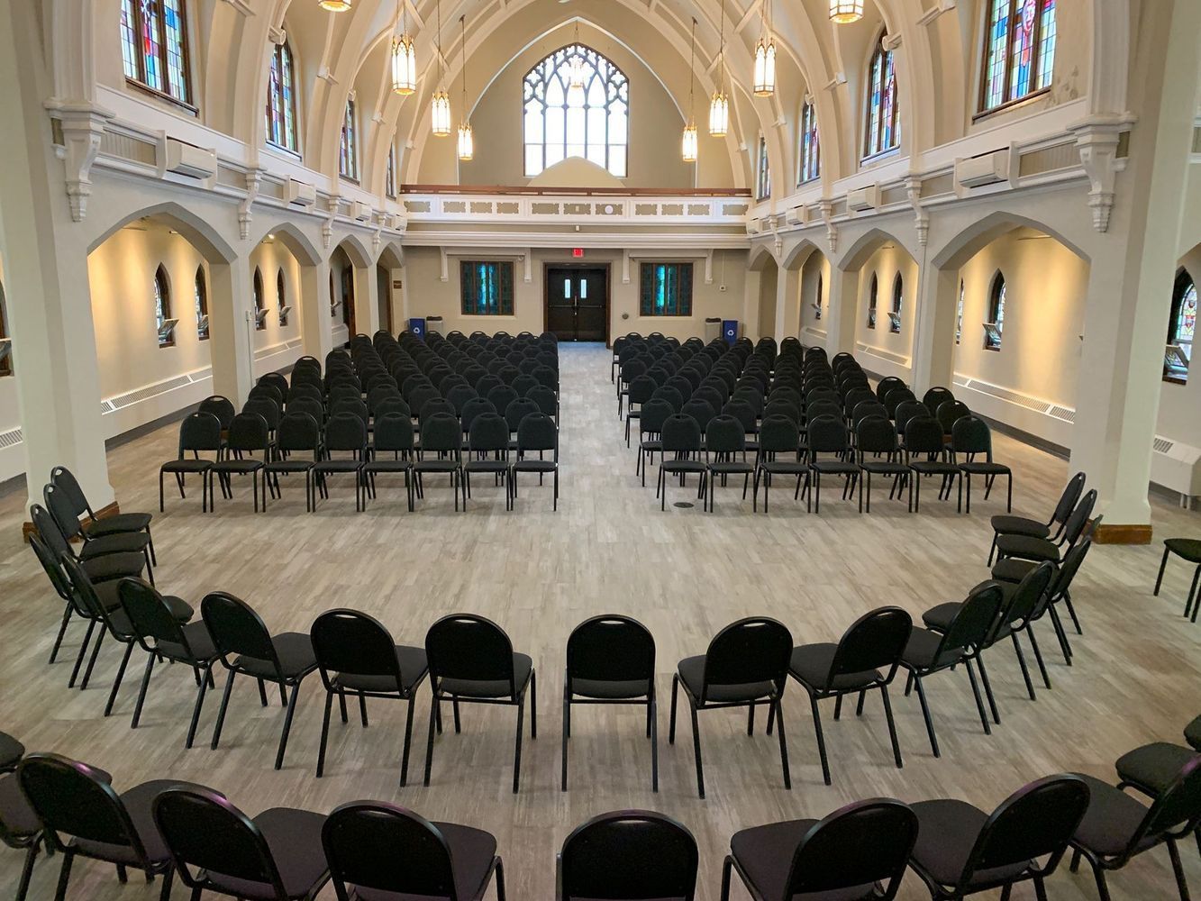 Interior of a church with rows of chairs facing a stage. Circle of chairs in front. Stained glass windows.