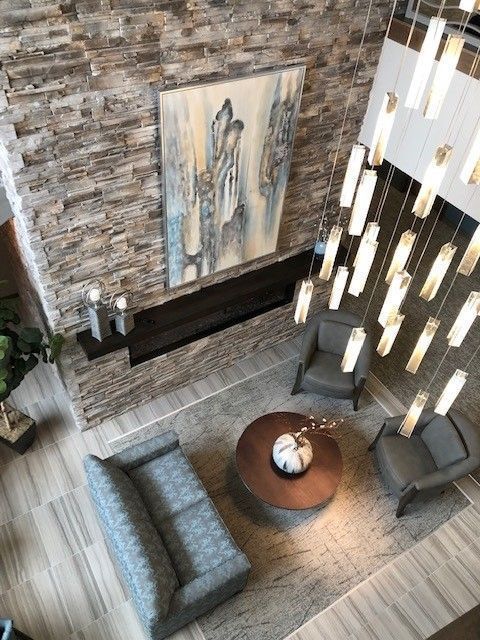 Lobby seating area: stone accent wall, artwork, sofa, chairs, round table, and a large chandelier.