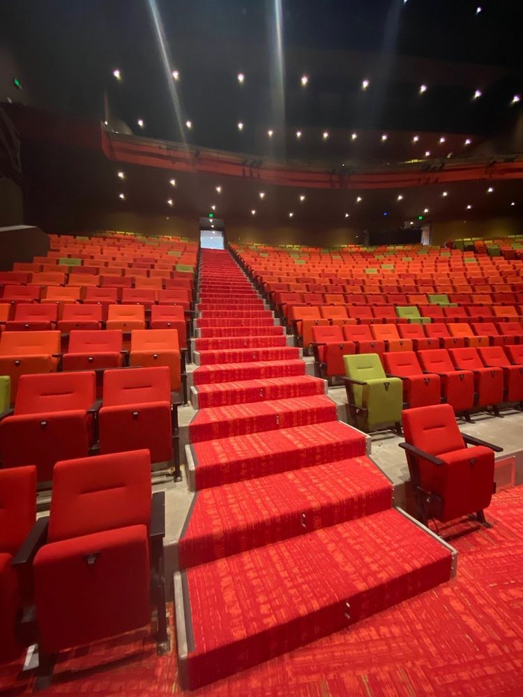 Red-carpeted steps ascend through empty red theater seating, leading to an exit. Some green seats are interspersed.