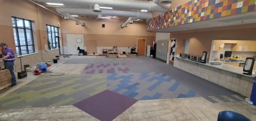 Interior of a room under construction with new carpet being installed. Workers, tools and materials are scattered around.