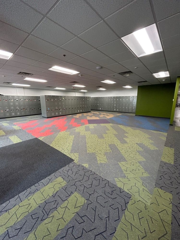 Empty locker room with gray lockers, colorful patterned carpet, and bright ceiling lights.