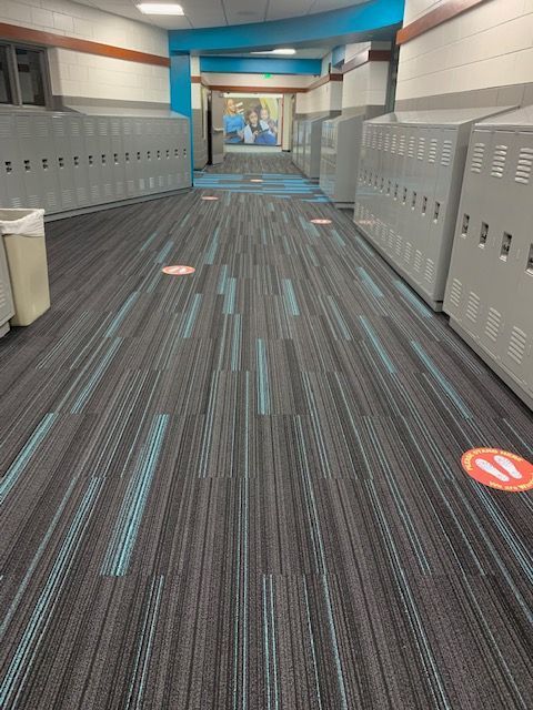 School hallway with lockers, patterned carpet, and social distancing markers.
