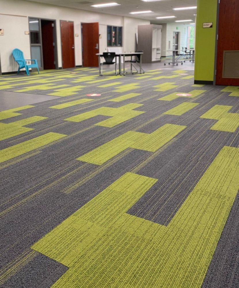 Large room with patterned green and gray carpet. Several closed doors and tables visible.