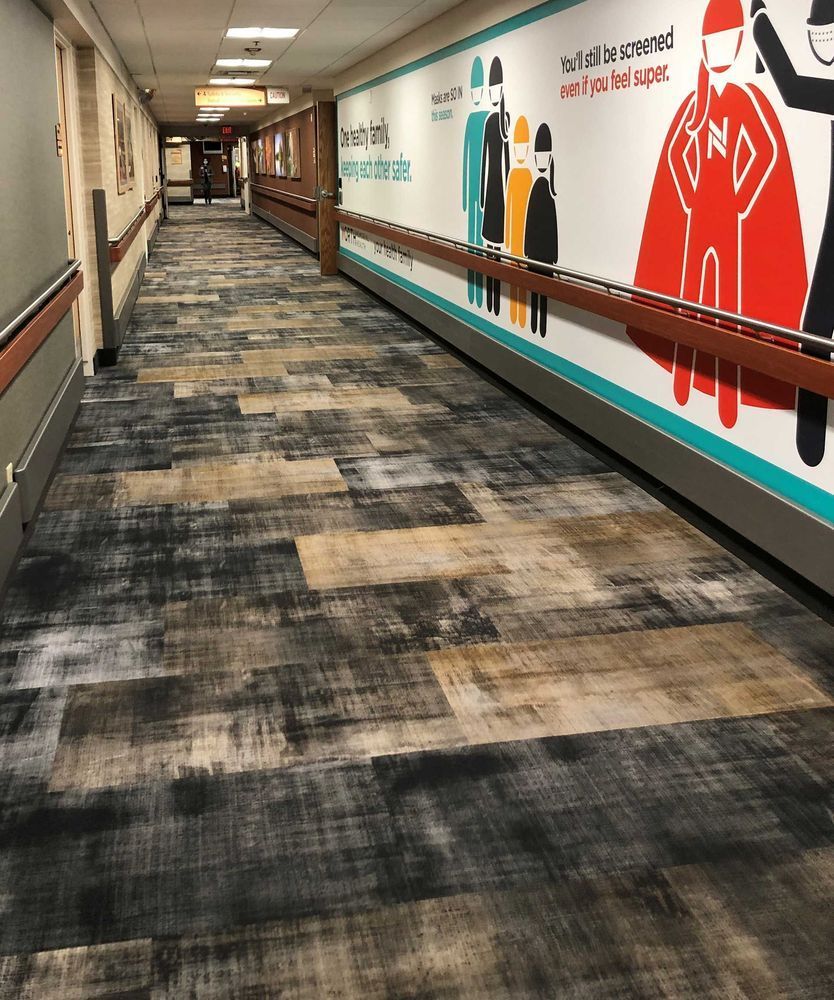 Hospital hallway with textured carpet, wall art, and handrails.