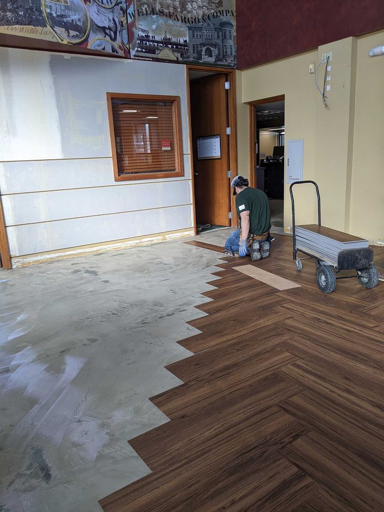 Worker installing brown herringbone flooring in a room. Partial flooring laid. Interior with partially painted walls.