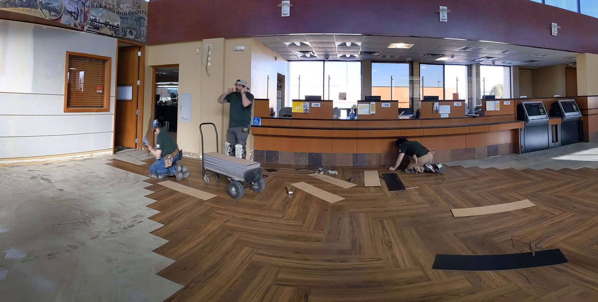 People installing wood flooring in a large, open commercial space with a curved counter and windows.