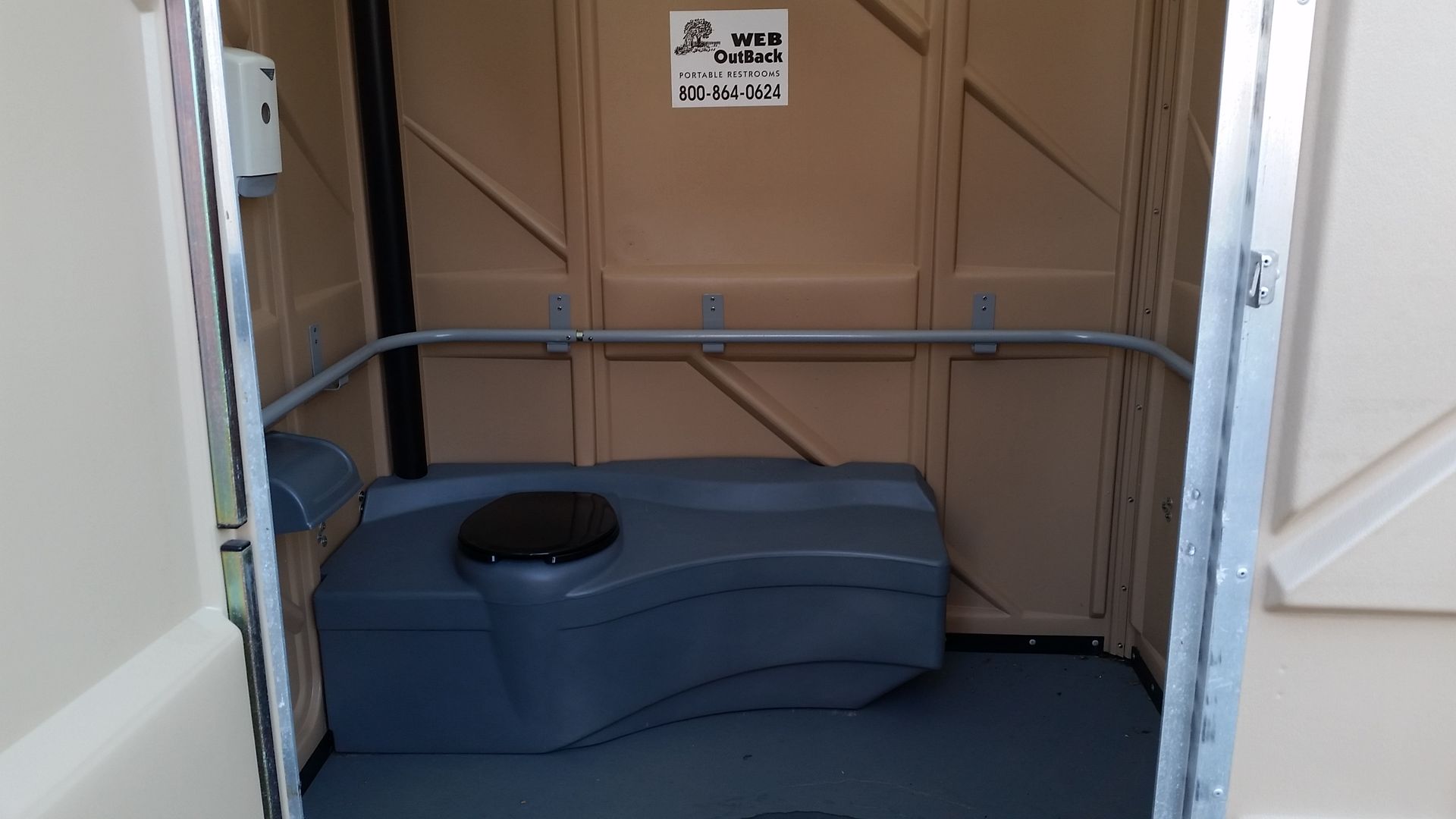 Portable toilet stall interior with a blue bench and black toilet opening, viewed through open white doors