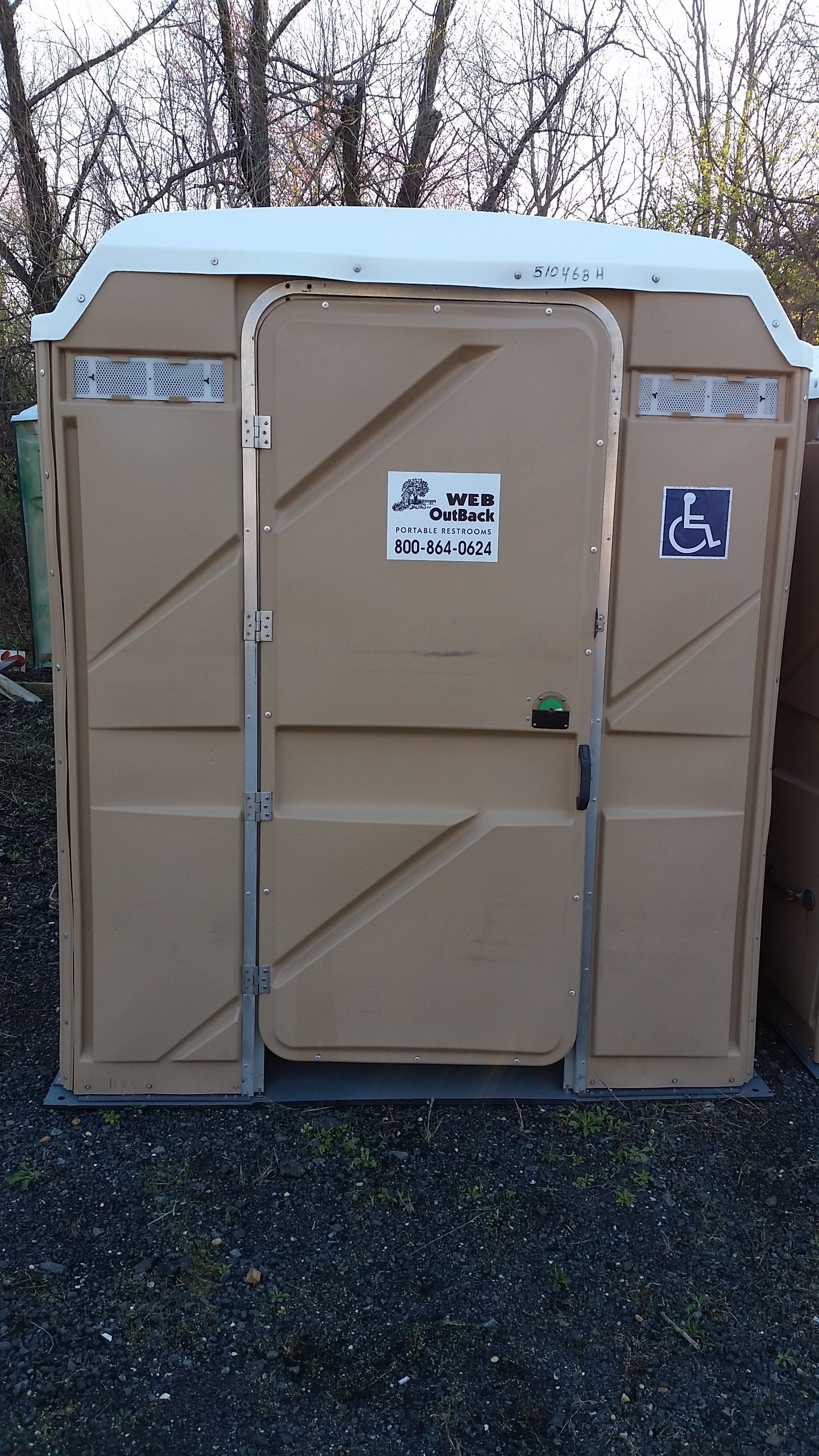 Beige portable toilet with blue roof sitting outdoors on gravel.