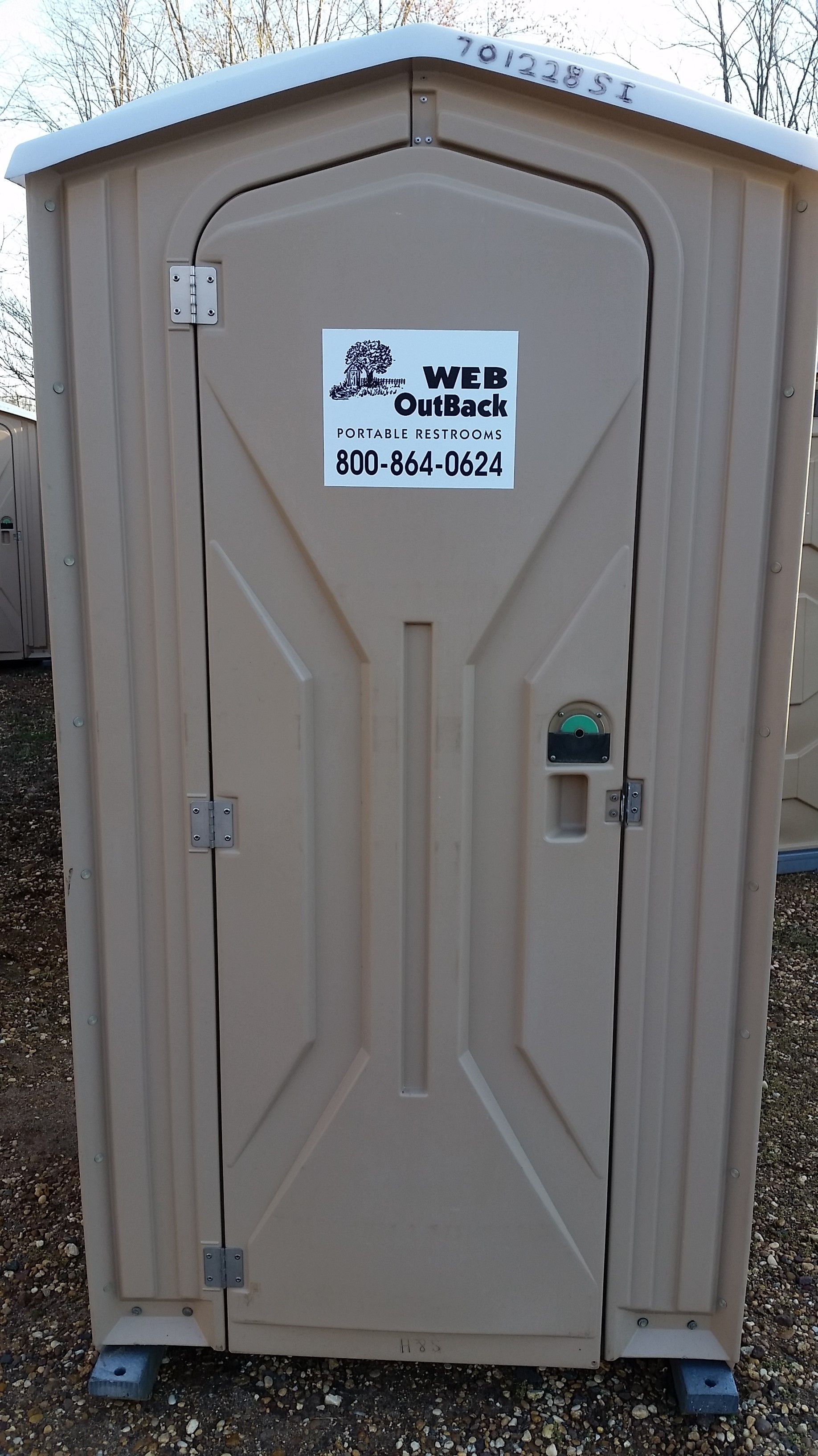 Beige portable toilet with a blue sign on the door, standing outdoors on gravel.