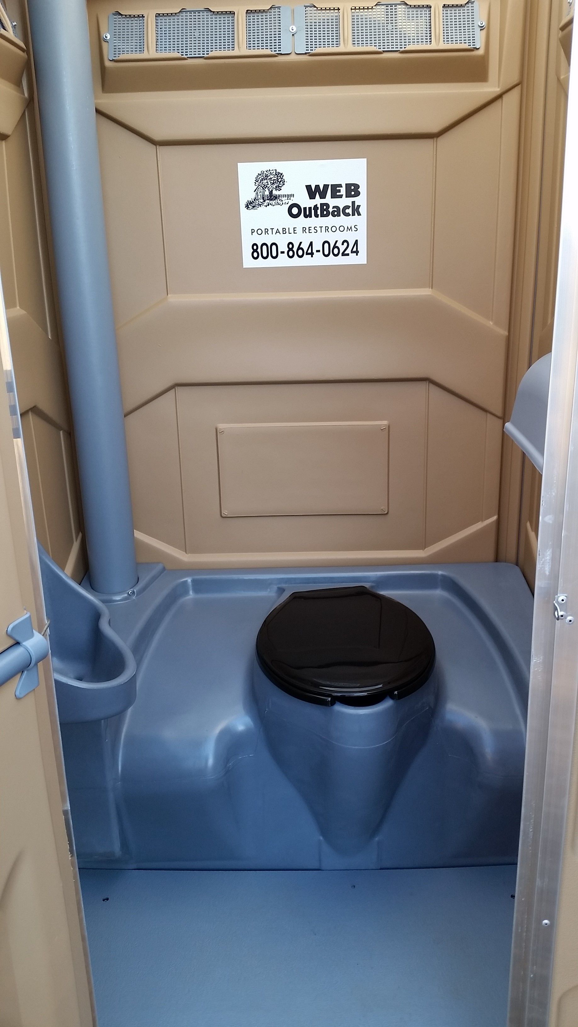 Portable toilet stall with a black seat and blue floor, viewed from the doorway