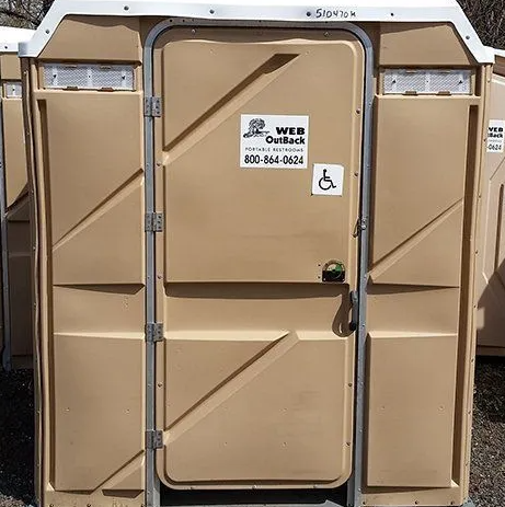 Tan porta-potty with a white top, a door with a wheelchair symbol, and a company logo.