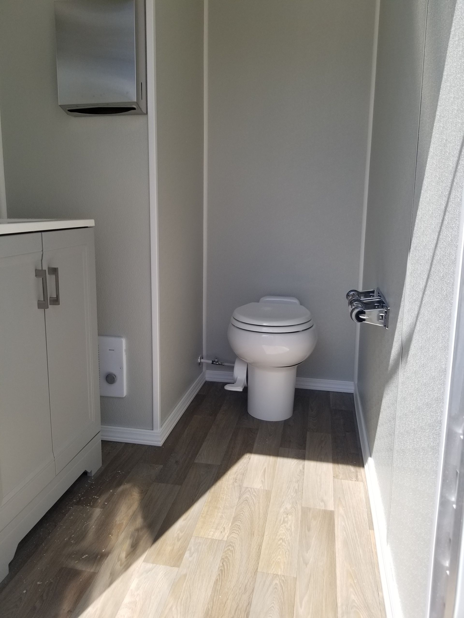 Interior of a portable restroom with a toilet, sink cabinet, and paper towel dispenser.