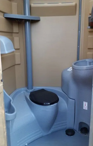 Interior of a beige and blue portable toilet. Features a toilet, sink, and soap dispenser.