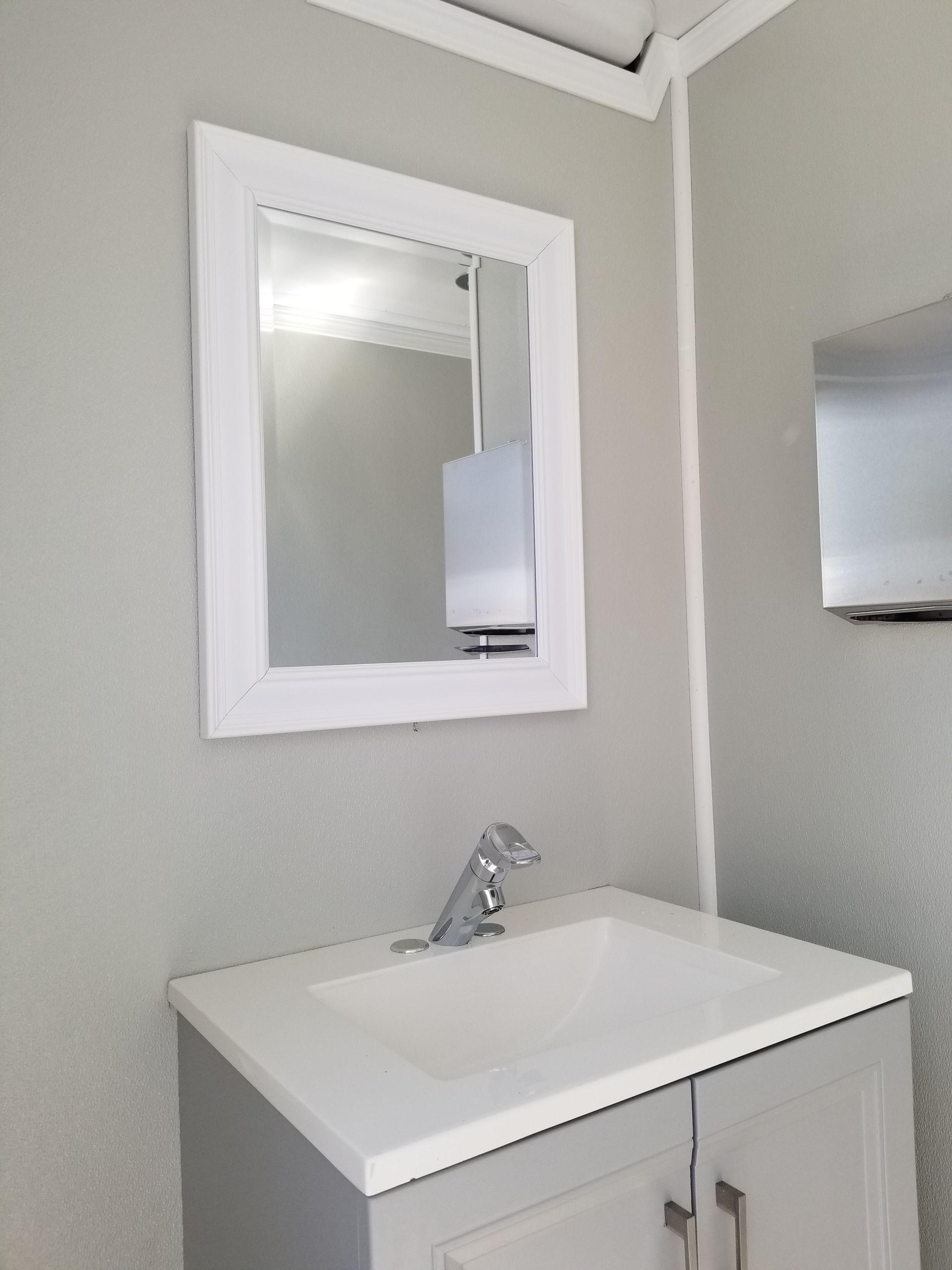 Bathroom sink with mirror in a white-framed cabinet, light gray walls, and silver faucet.