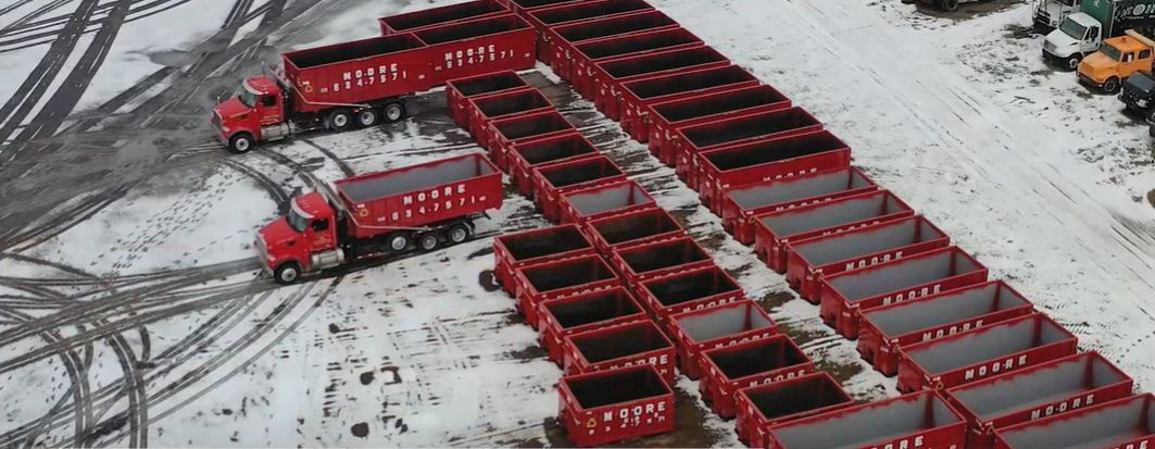 An aerial view of a row of red metal containers and dump trucks in the snow