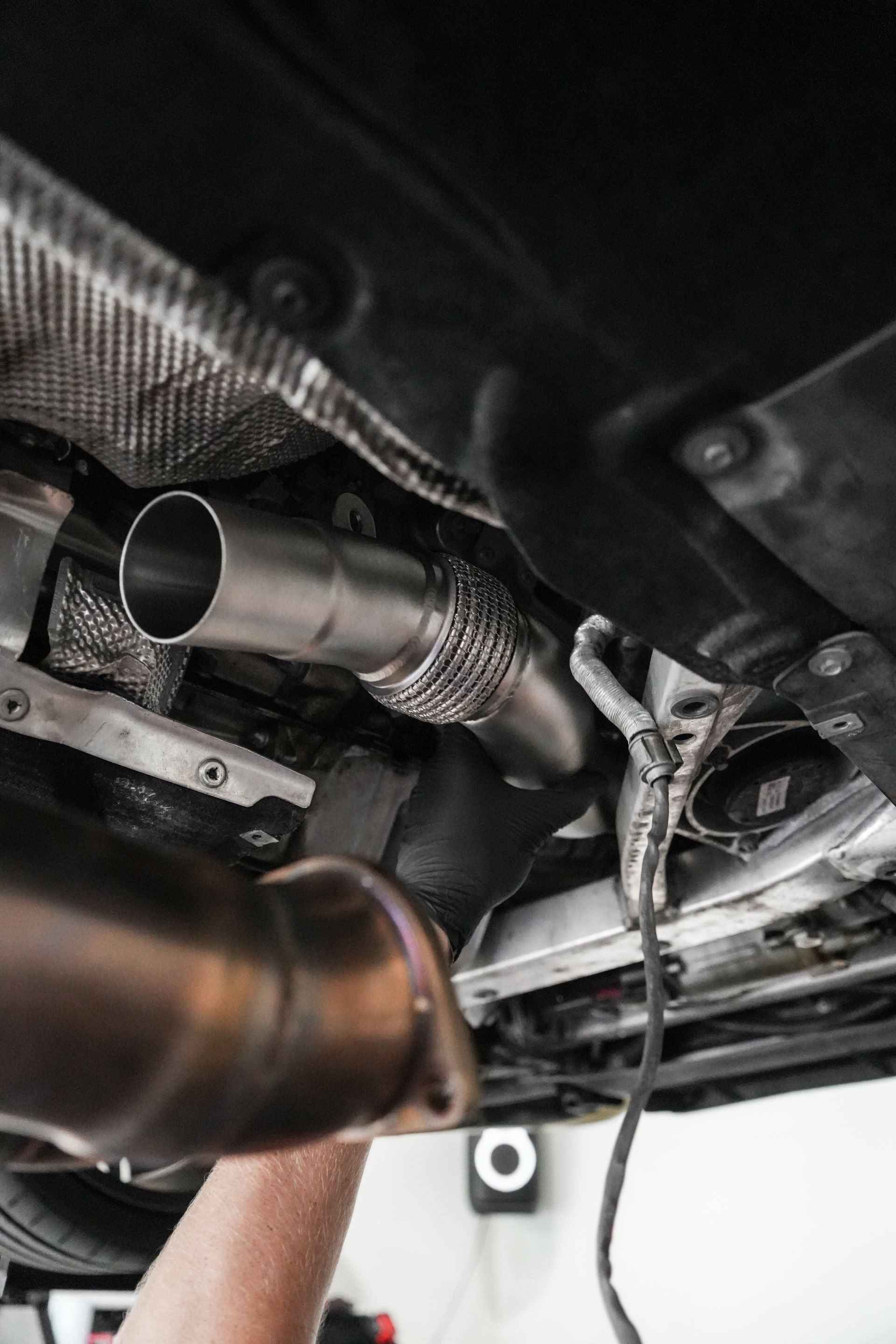Undercarriage view of a vehicle with exhaust pipes and heat shielding, shown during inspection or repair.