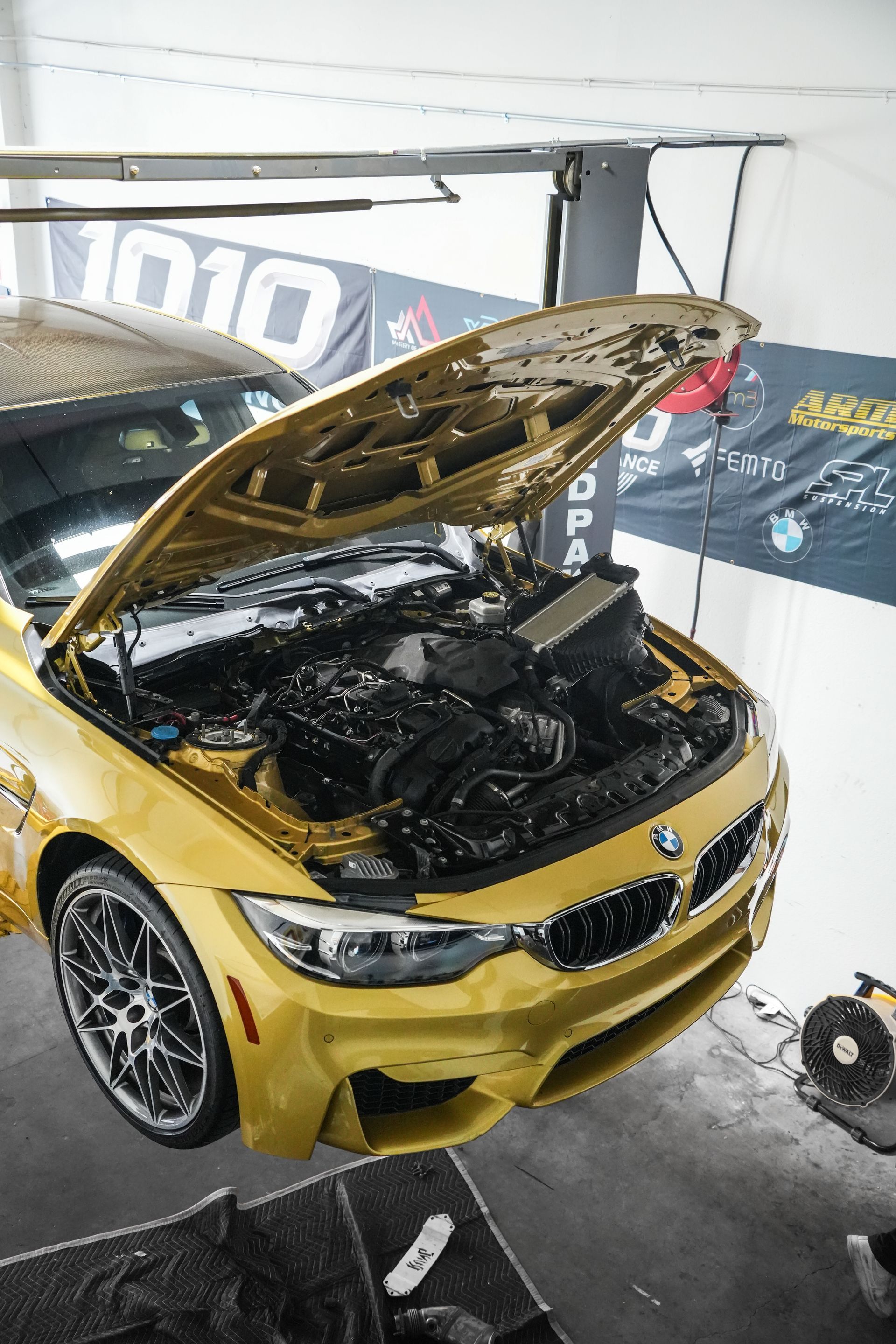 Yellow sports car with hood open, showing engine at an indoor display booth.