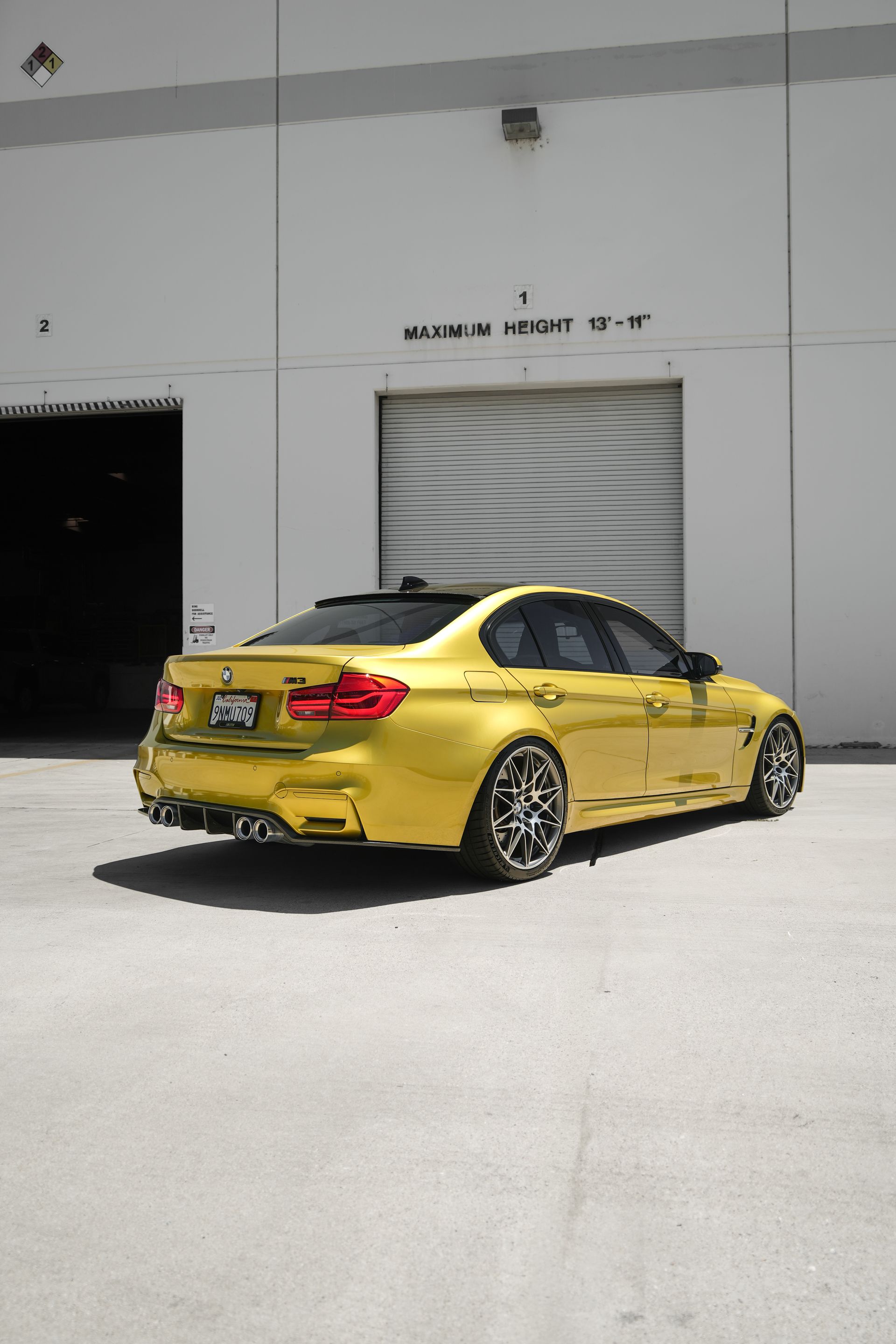 Yellow sedan parked outside a white industrial garage in bright sunlight.