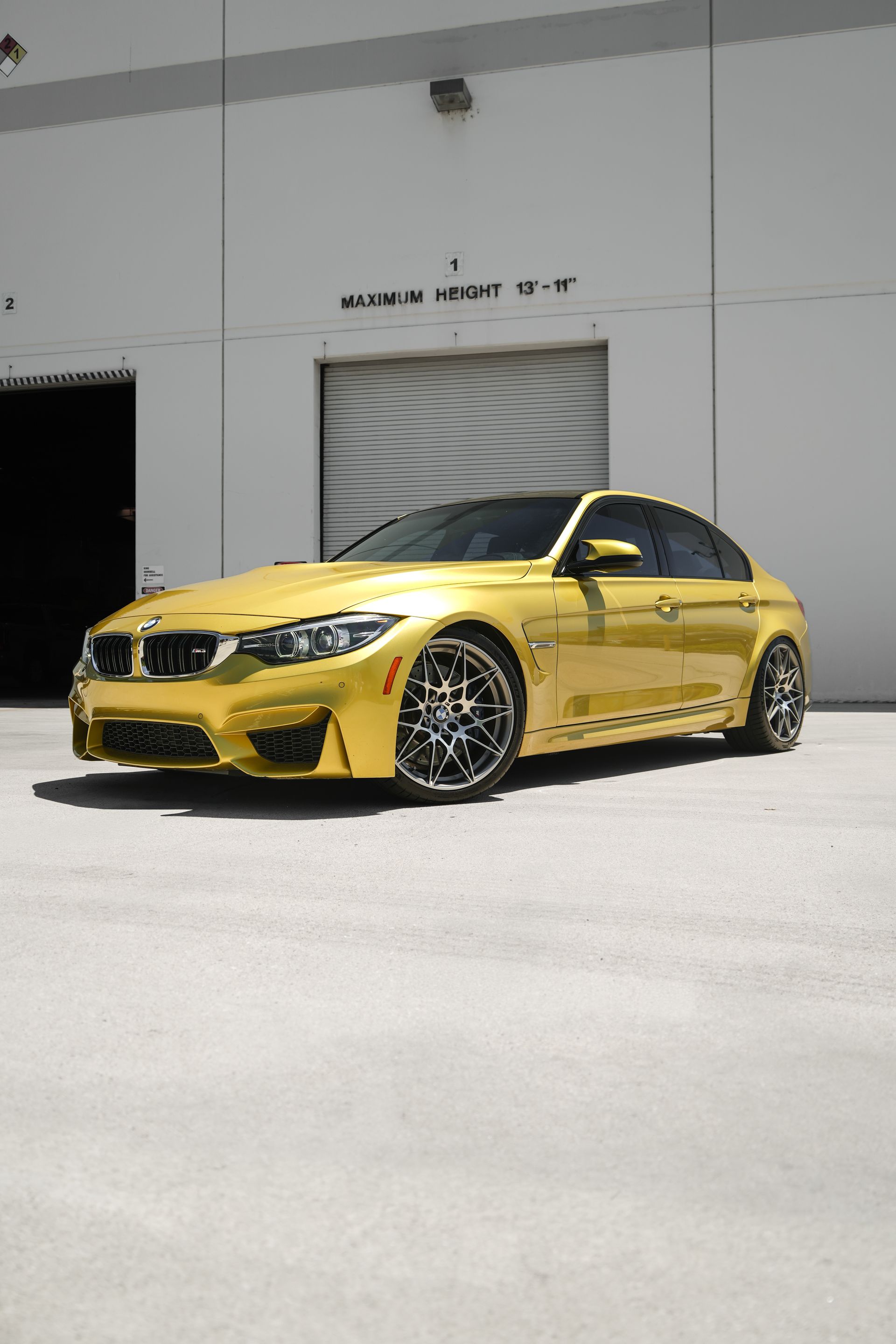 Yellow sports sedan parked outside a gray industrial building in bright sunlight