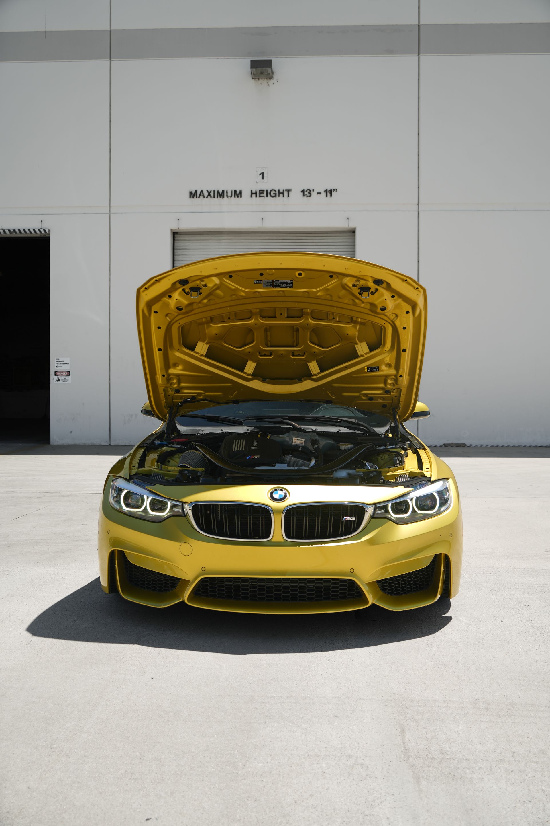 Yellow BMW with hood open parked outside a building.