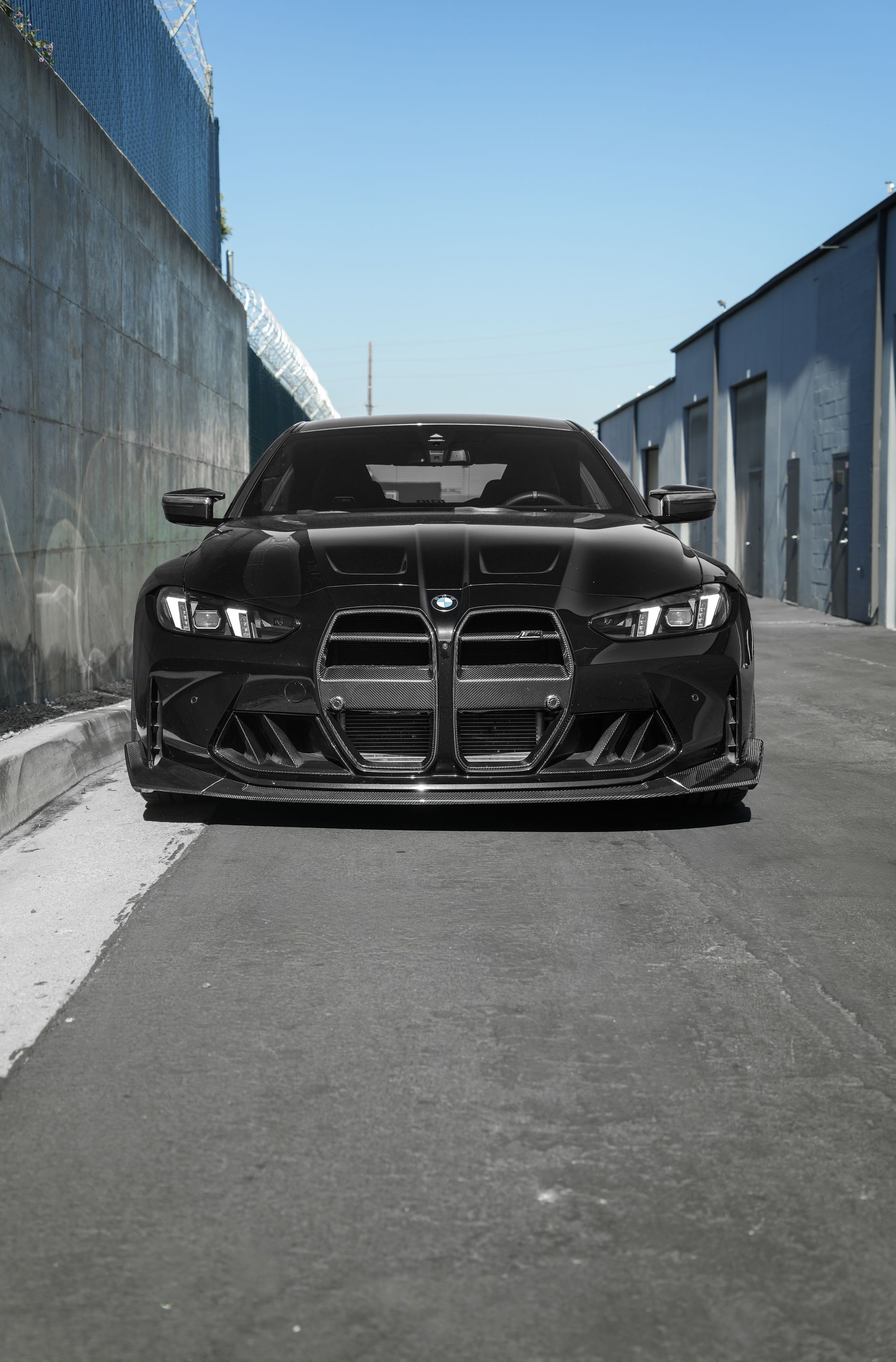 Black sports car parked in a narrow alley between industrial buildings under a clear blue sky