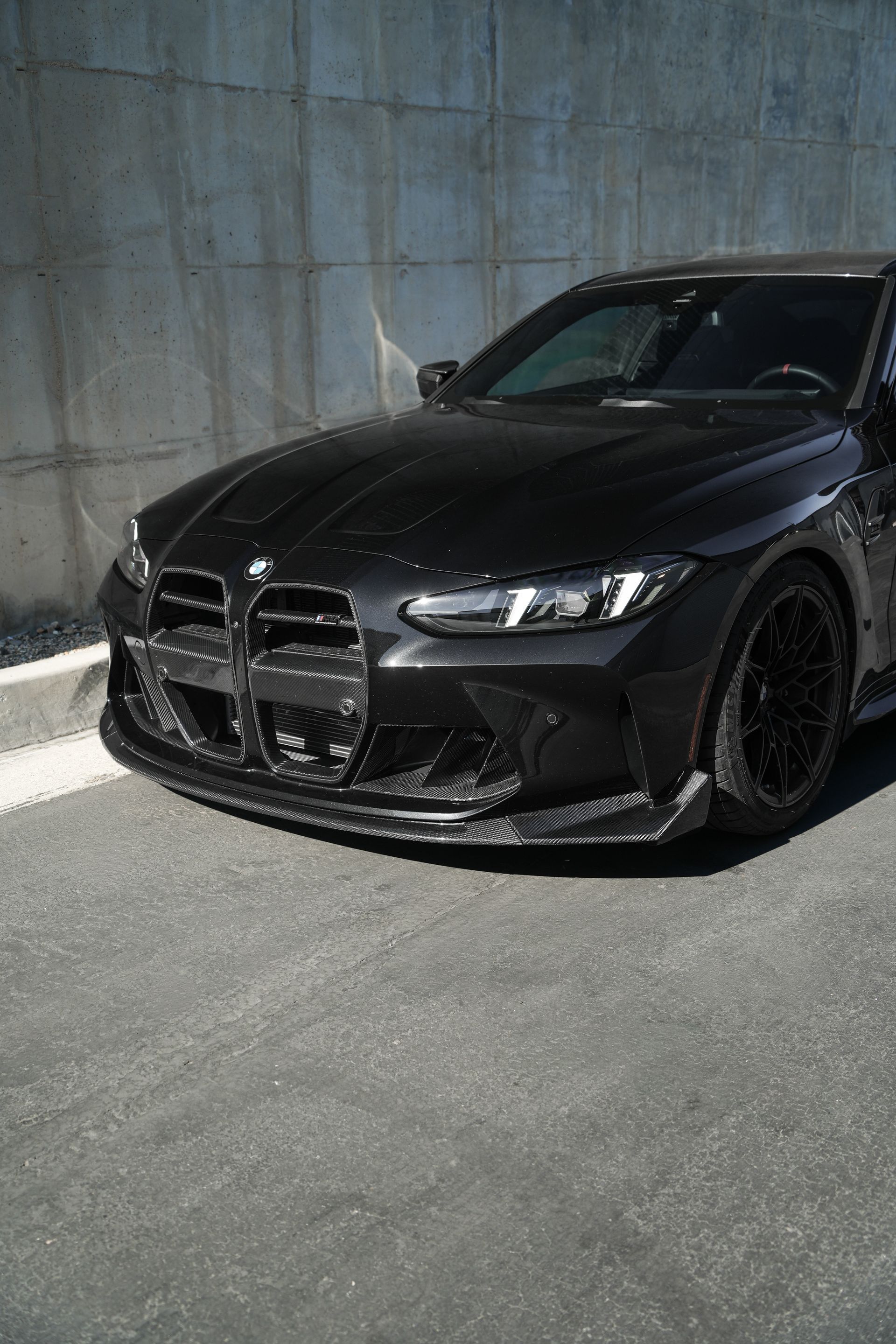 Black BMW sedan parked beside a concrete wall in bright sunlight.