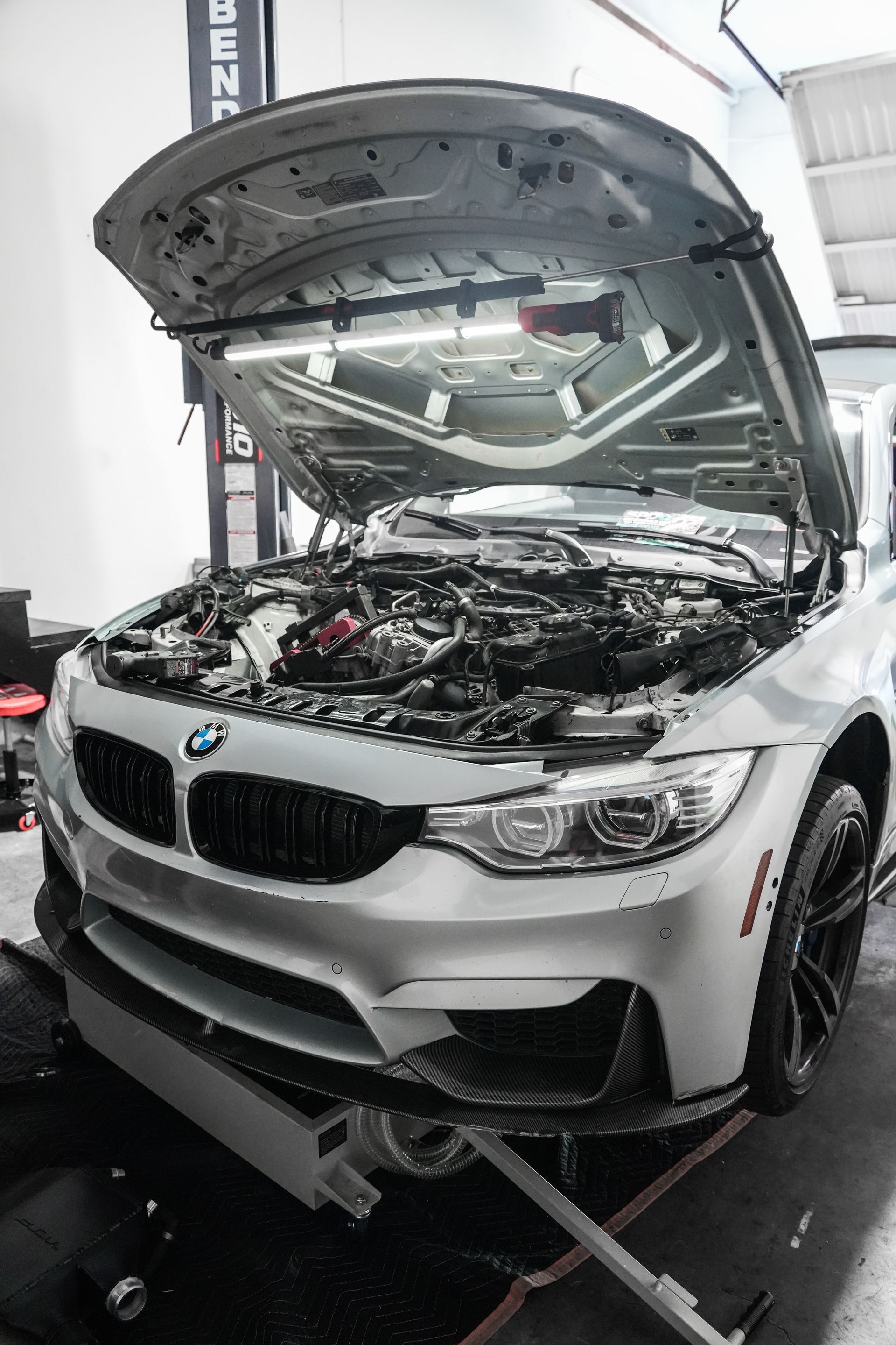White BMW with hood open in an auto shop, exposing the engine for repair.