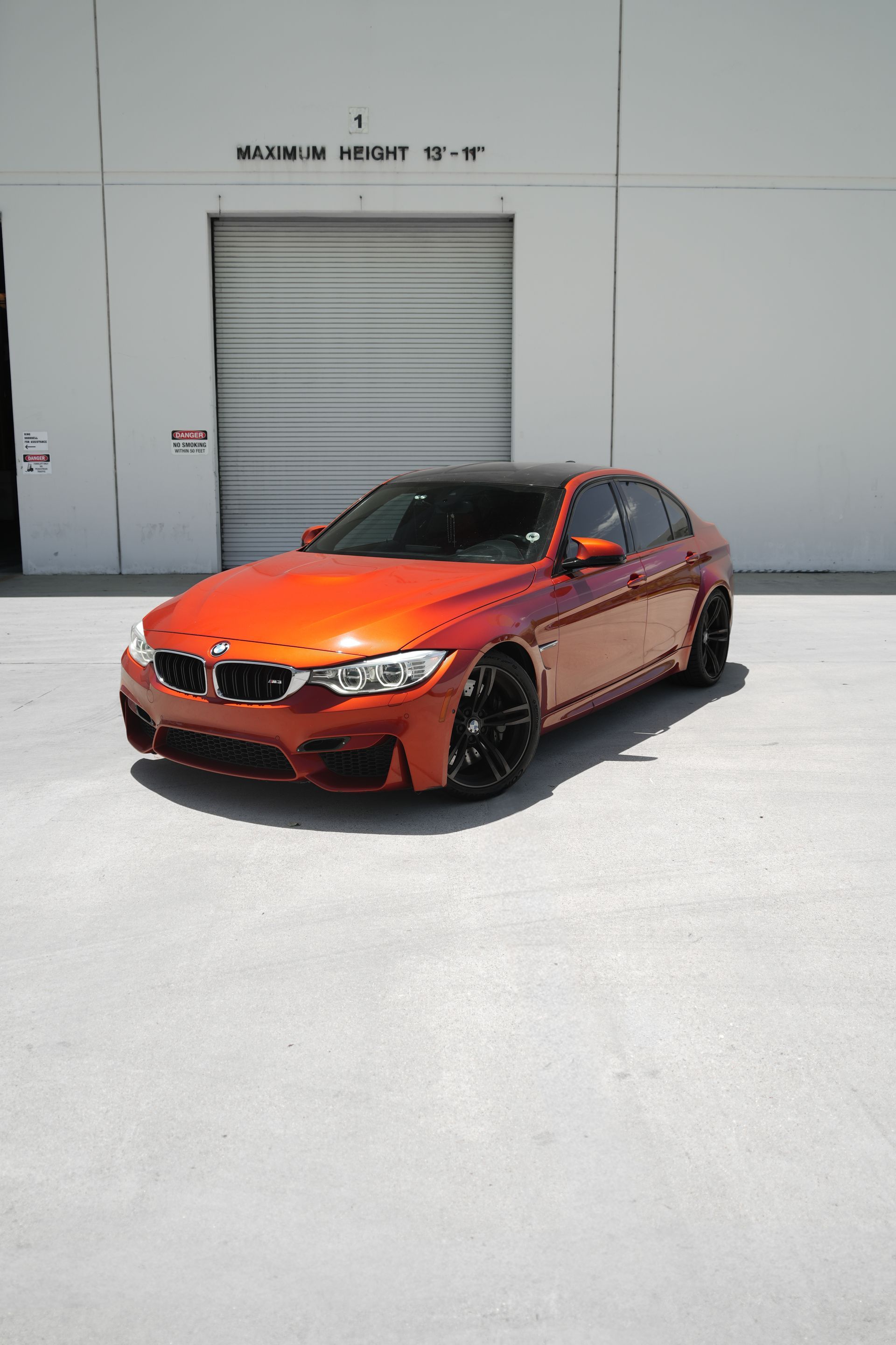 Orange sports sedan parked in front of a gray industrial garage door on a bright day