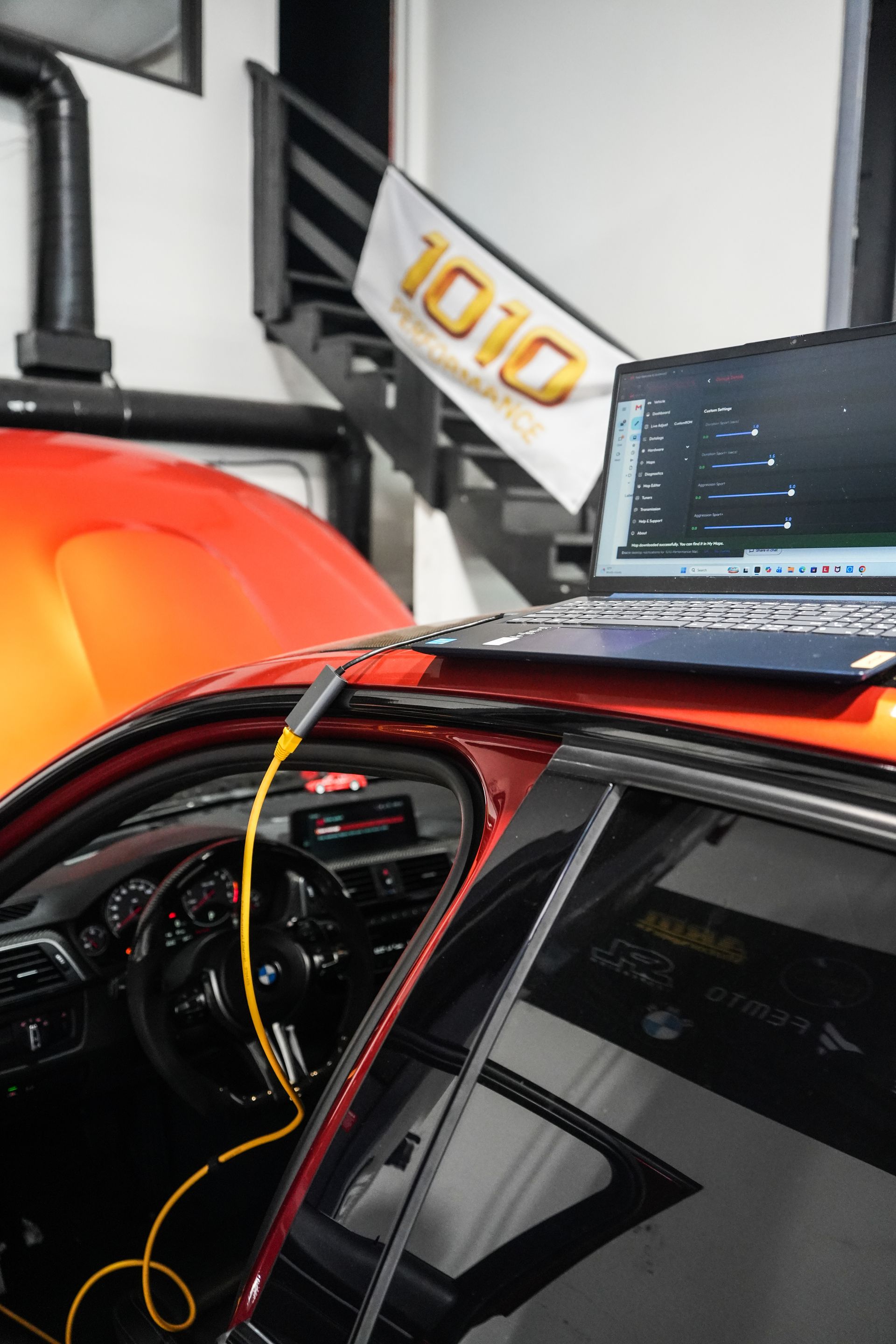 Laptop mounted inside a red race car garage interior, with cables draped over the door.
