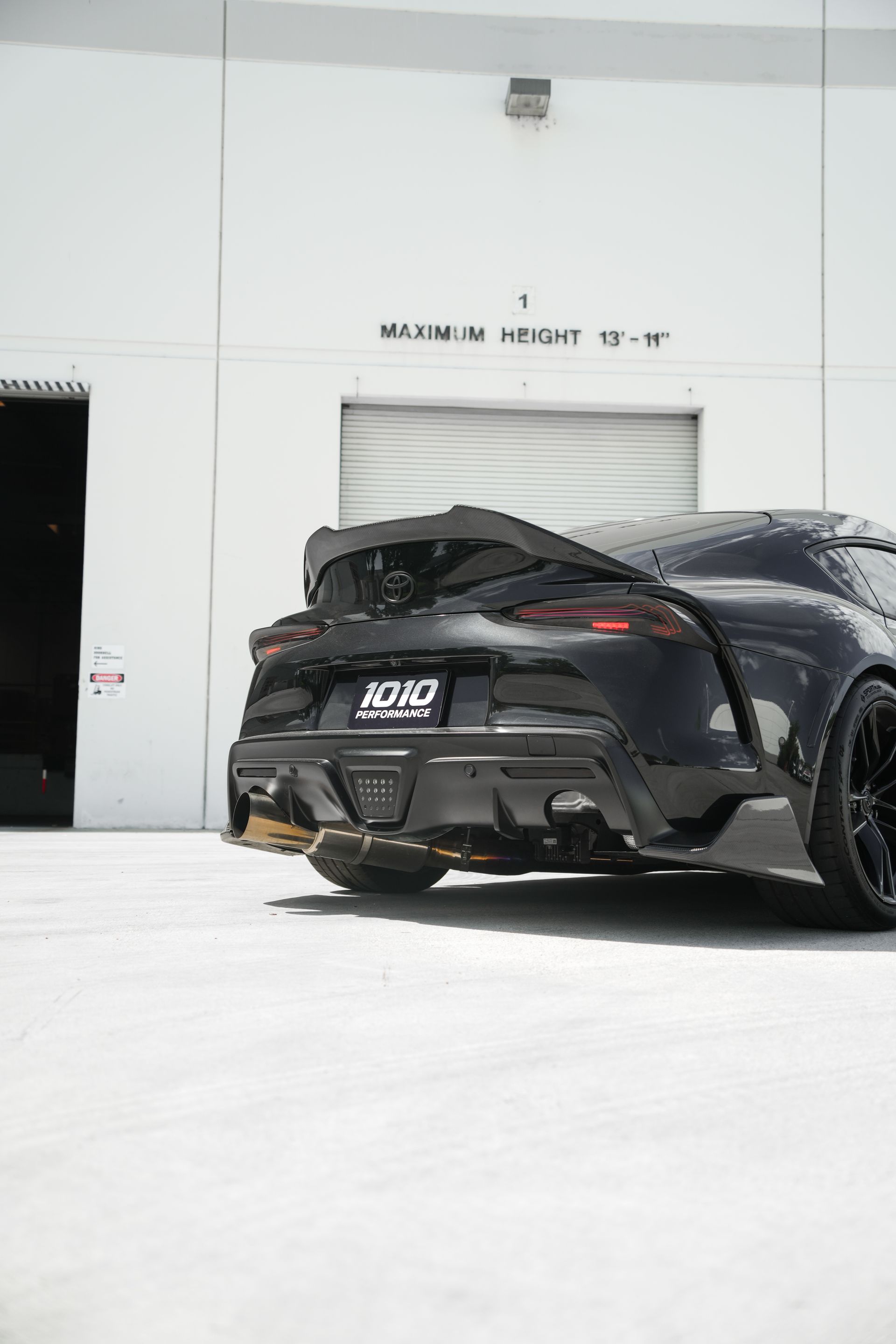 Black sports car parked outside a white building with a large garage door