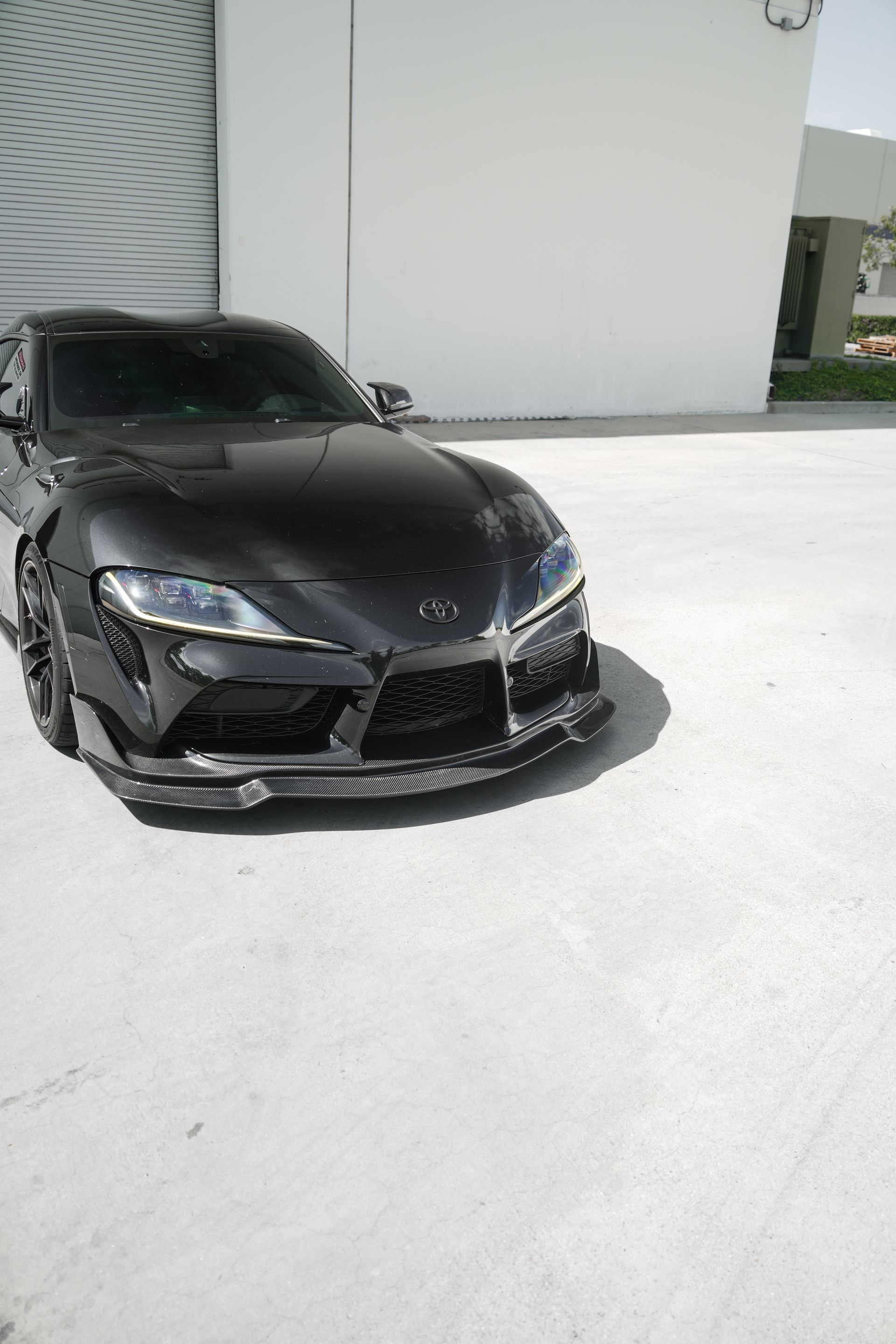 Black sports car parked on a bright concrete surface beside a white building.