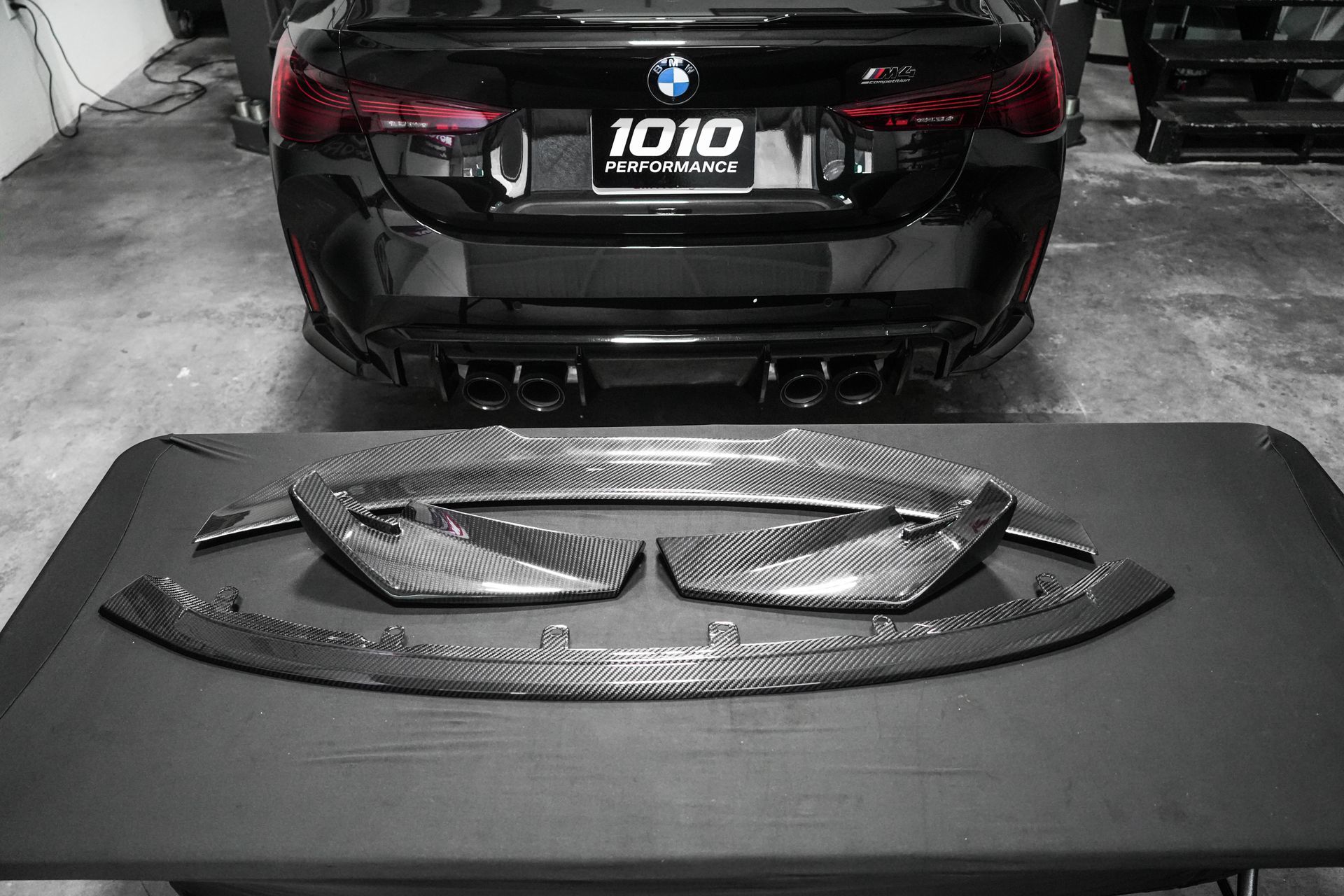 Black car with aftermarket front grille parts laid out on a black table in a garage.