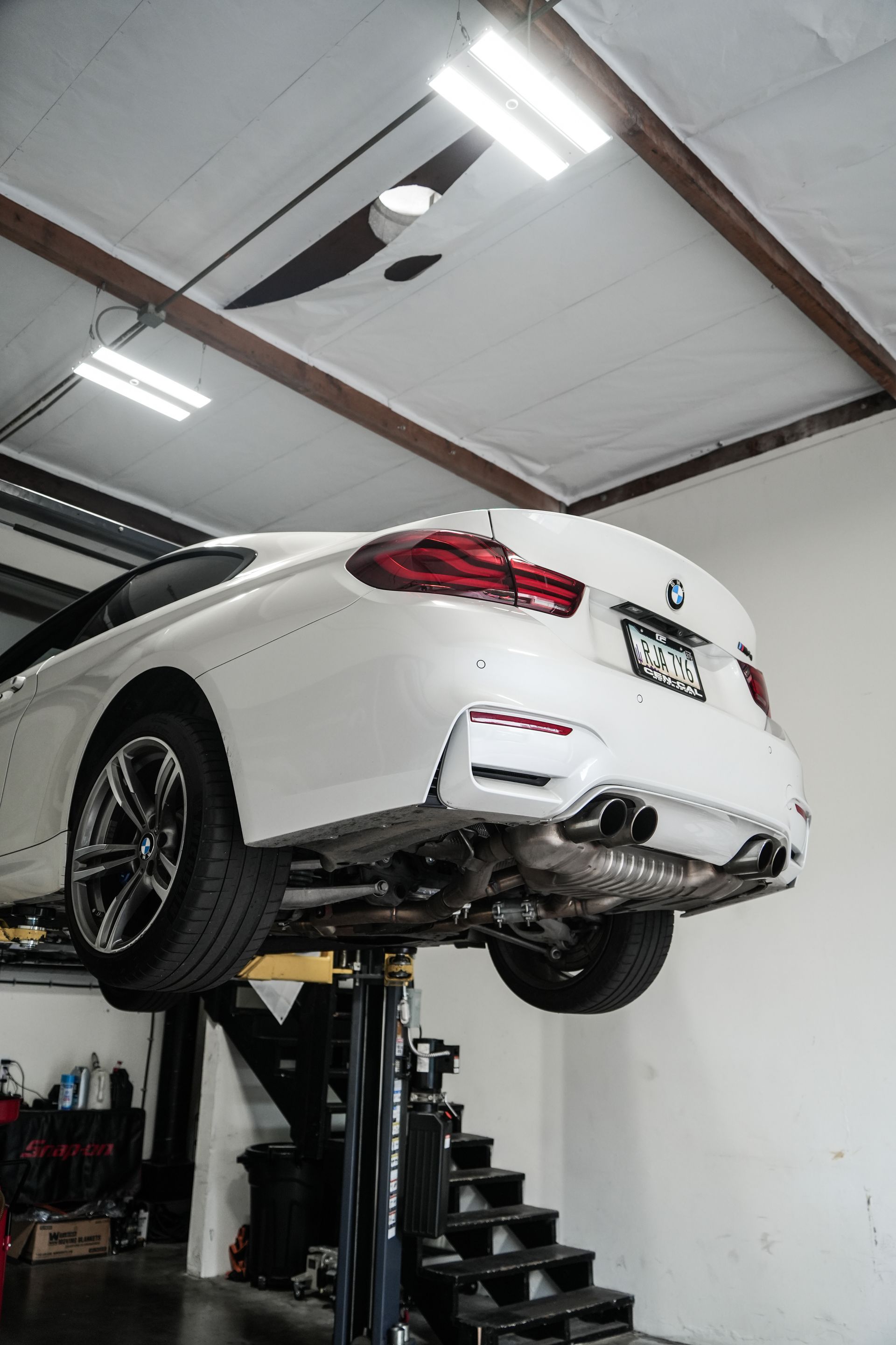 White sports car raised on a lift in an auto repair shop with stairs beside it
