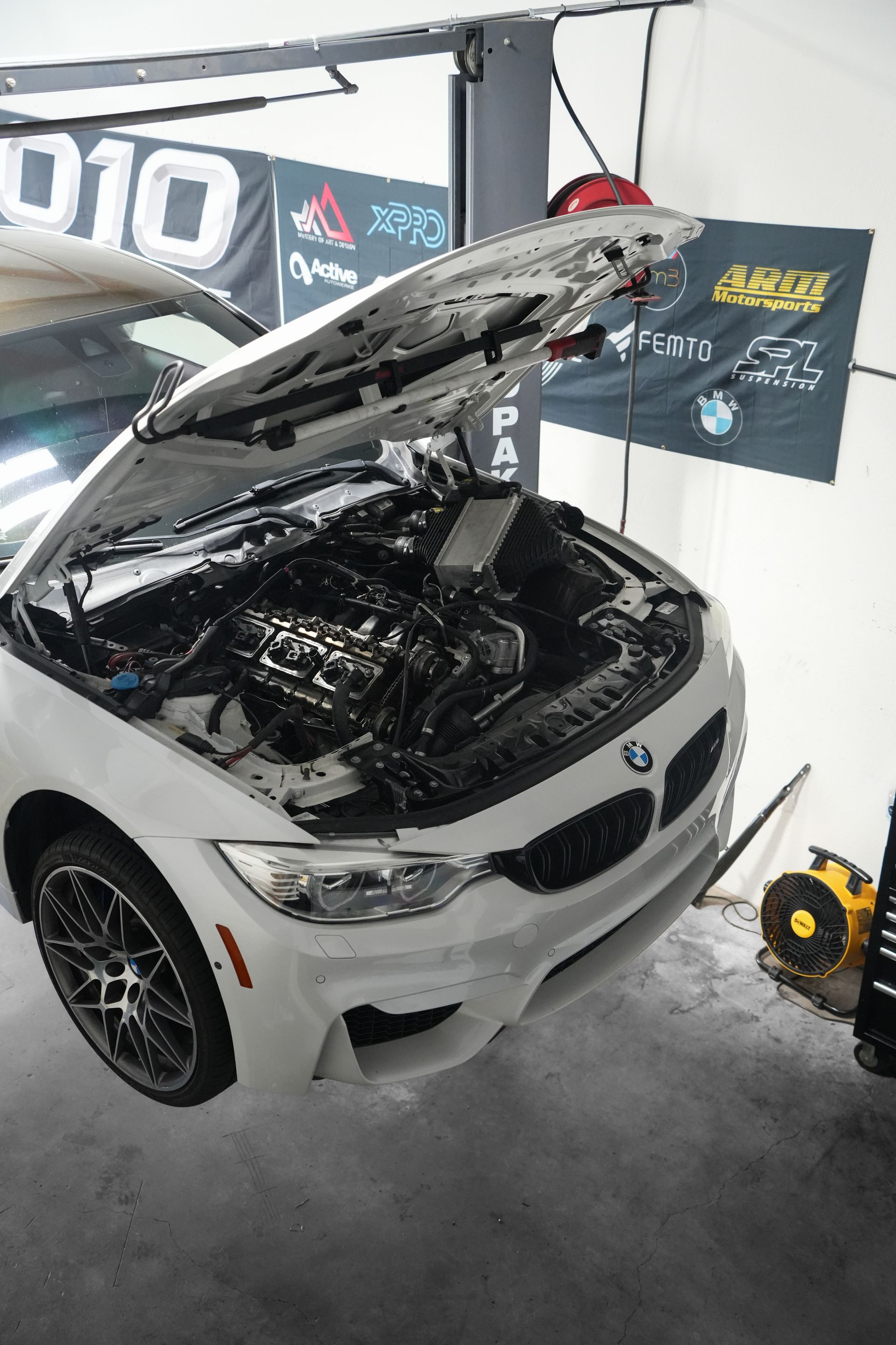 White BMW in garage with hood open, showing the engine bay during maintenance.