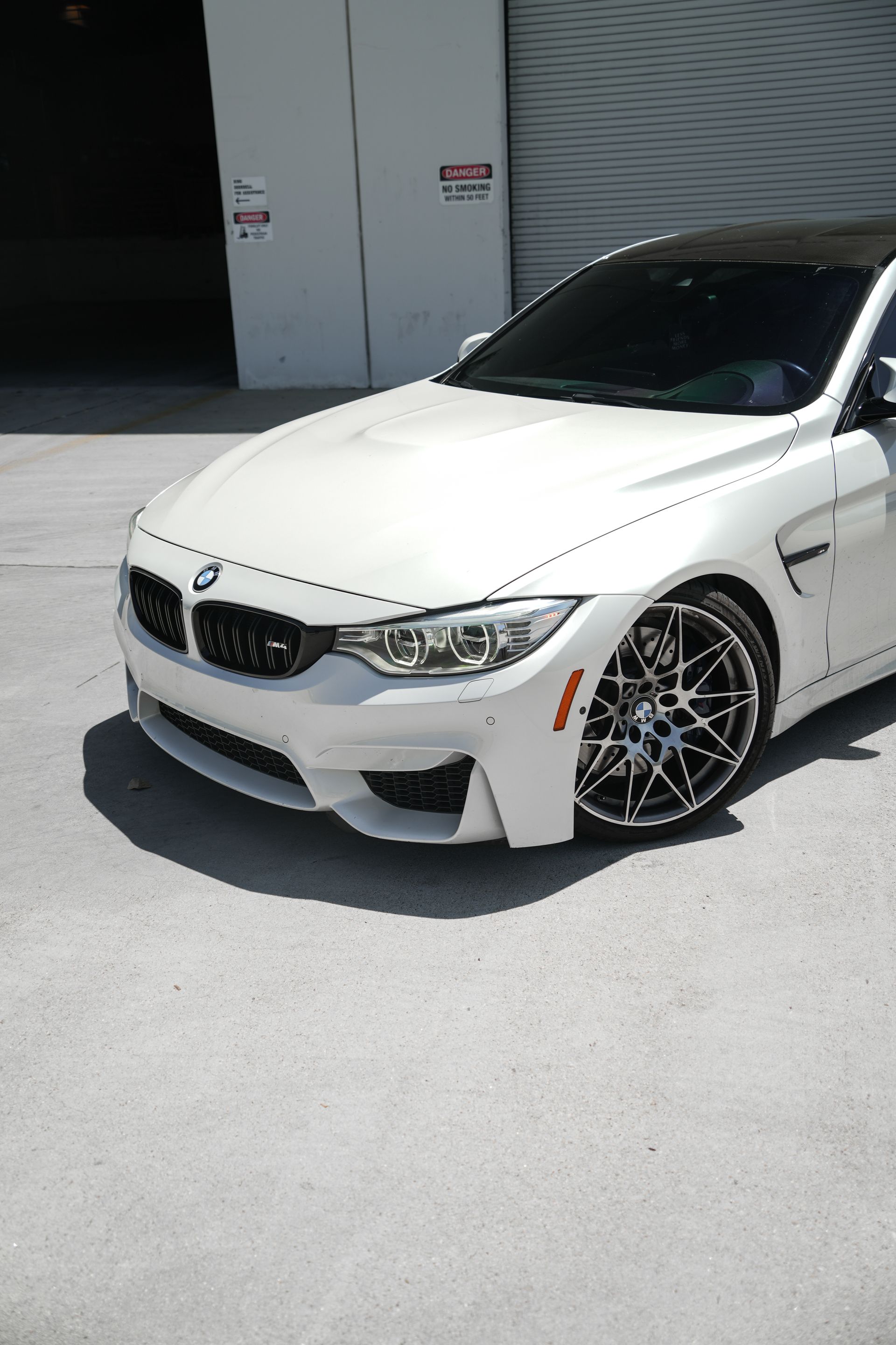White BMW coupe parked outside a building, front angle with custom black wheels.
