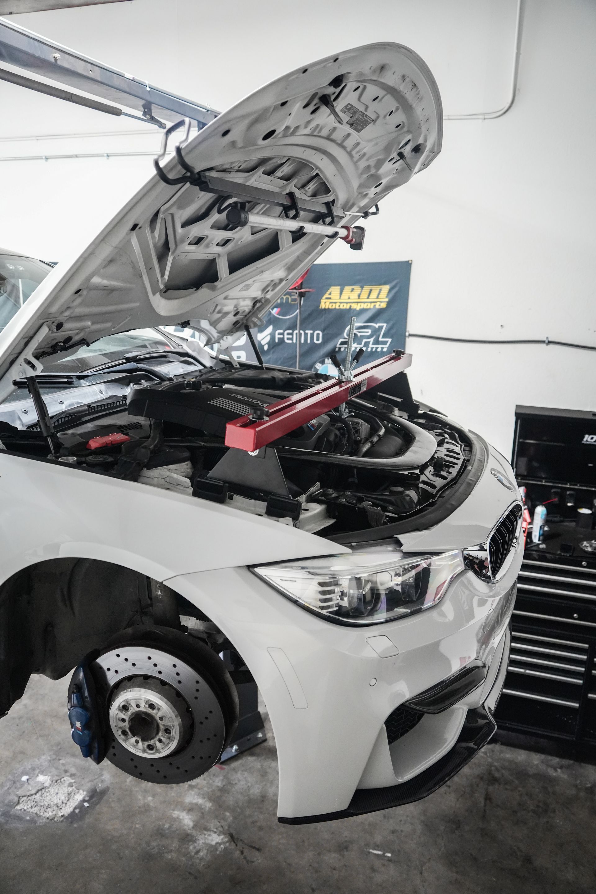 White car with hood open in an auto shop, engine exposed and repair tools nearby