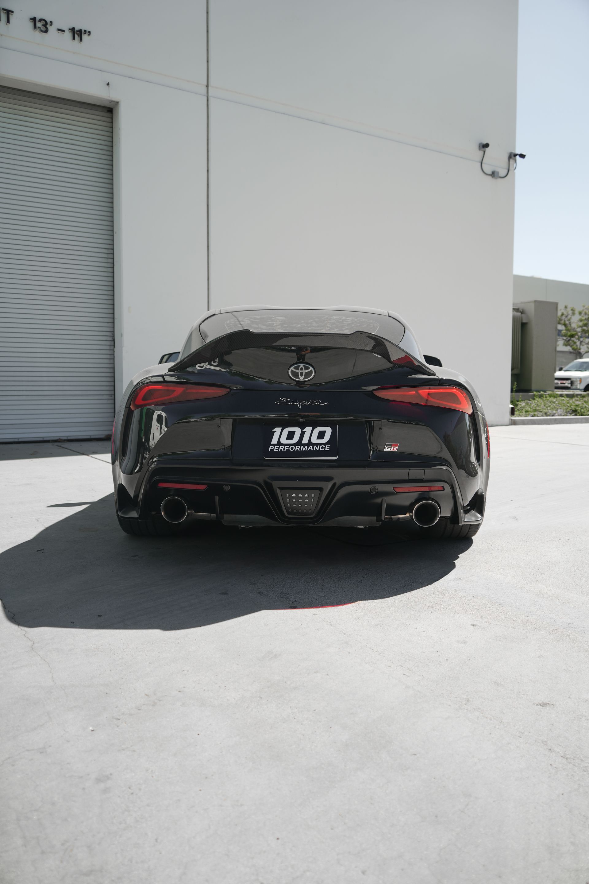 Black sports car parked beside a white building on a sunny day