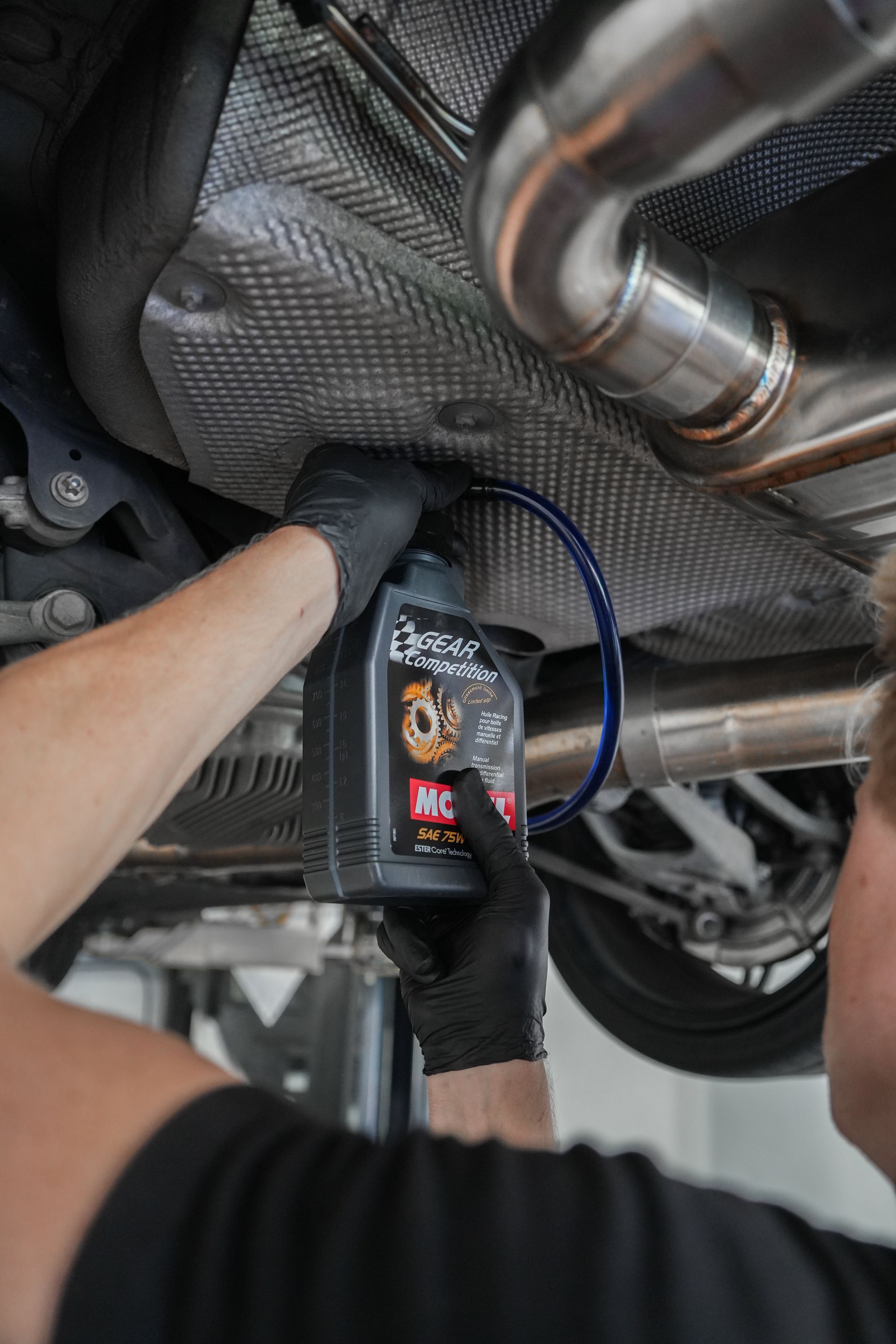 Mechanic using a diagnostic tool under a car’s exhaust and heat shield in a workshop
