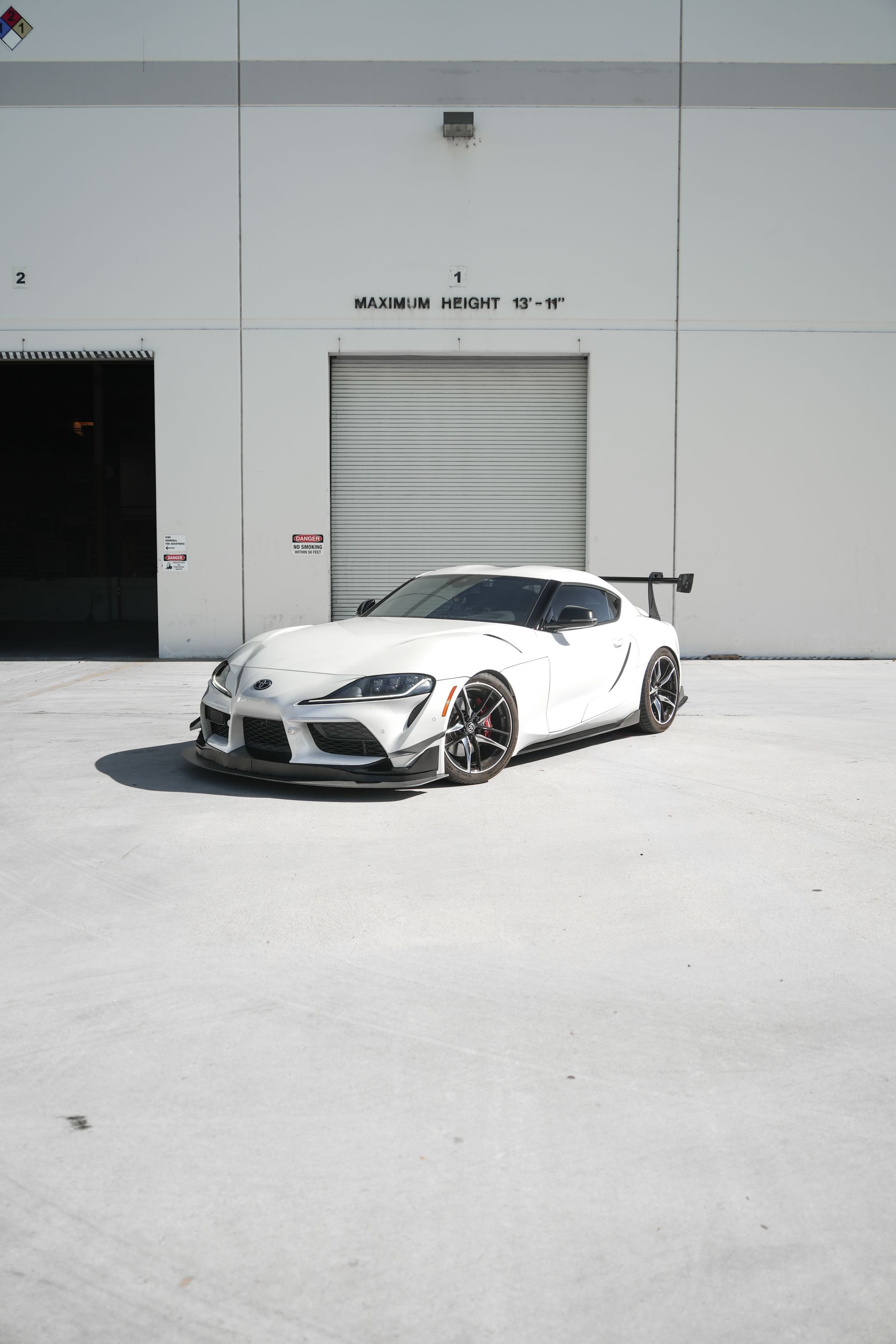 White sports car parked outside a gray warehouse in bright sunlight