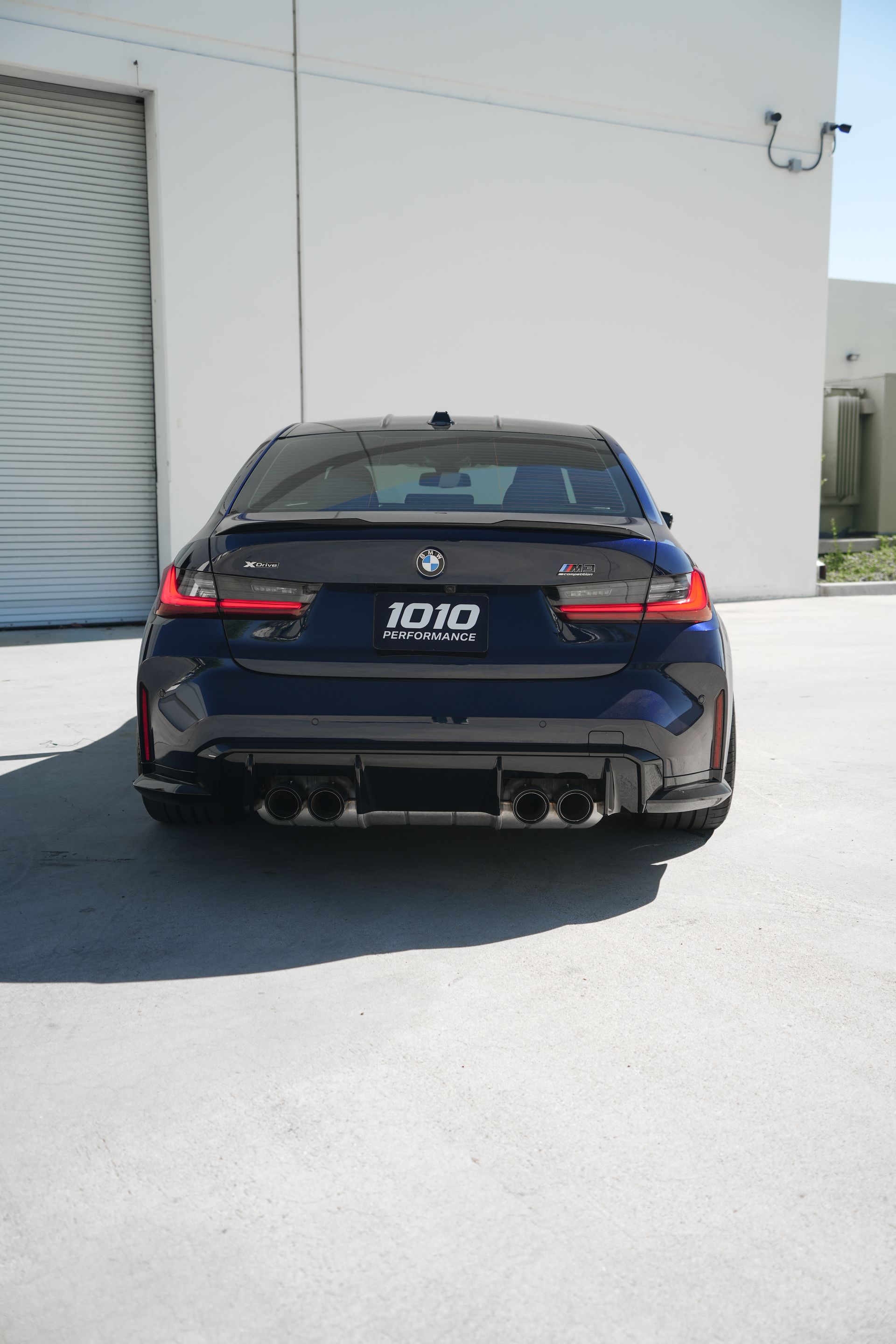 Rear view of a dark blue sports sedan parked by a white industrial building.