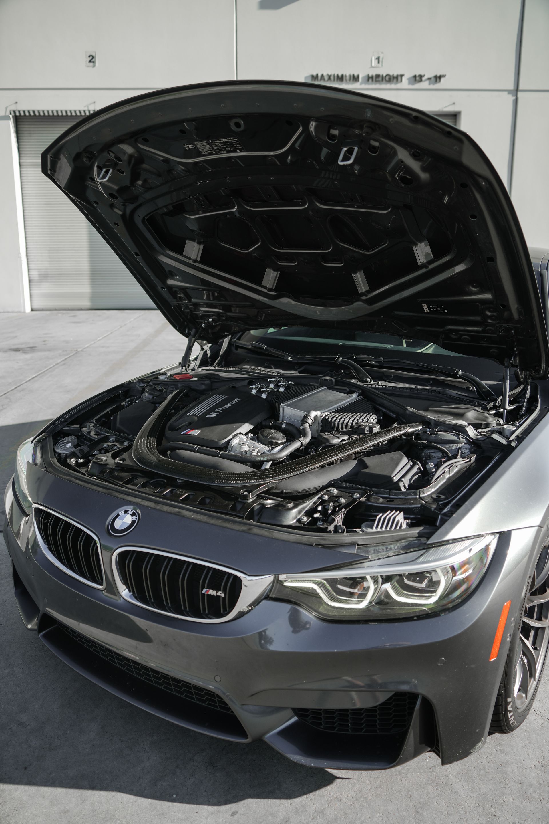 Gray BMW with hood open, showing the engine in a garage.