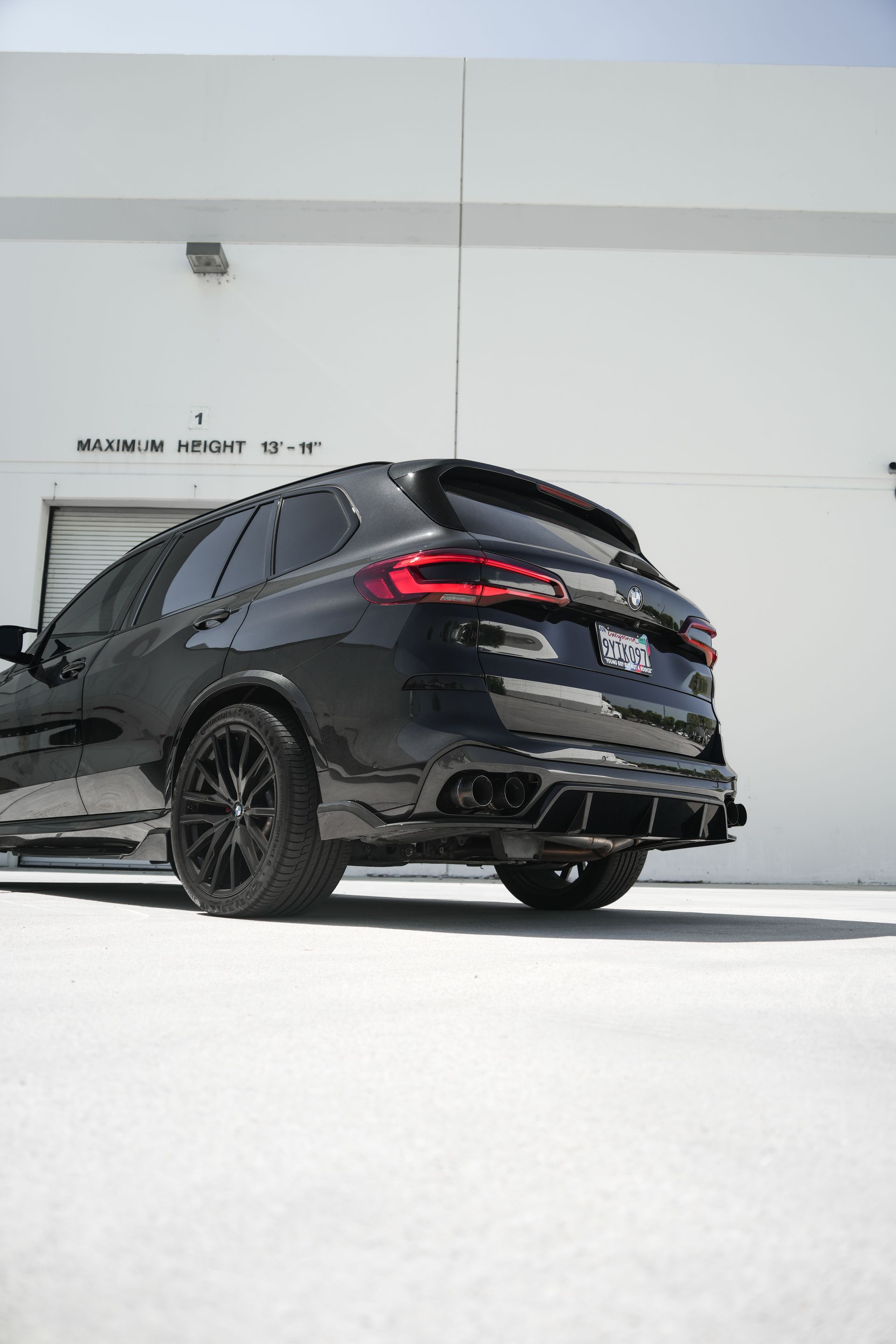 Black SUV parked outdoors beside a white building, shown from the rear at a low angle.