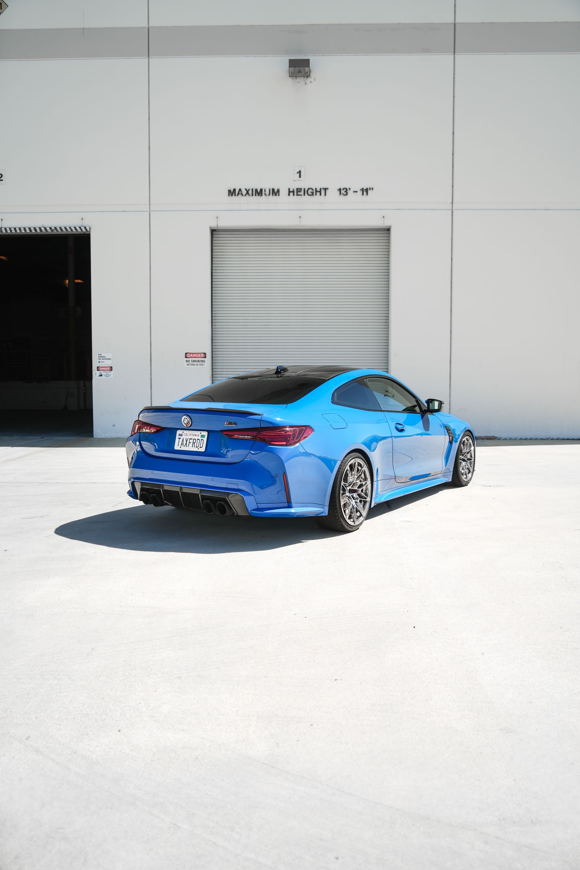 Blue sports car parked outside a white industrial building in bright sunlight