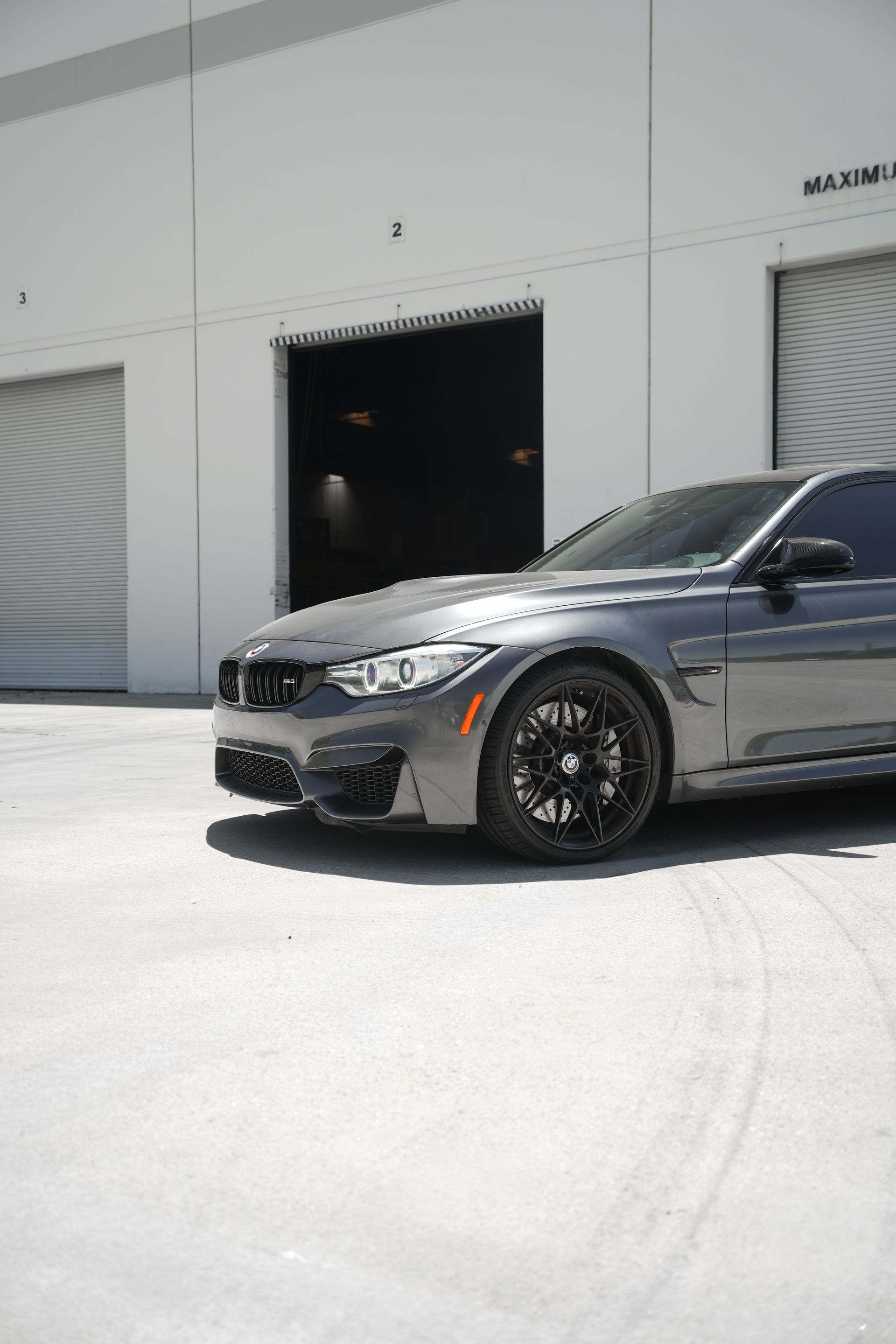 Black sedan parked outside a white industrial building with an open garage door.