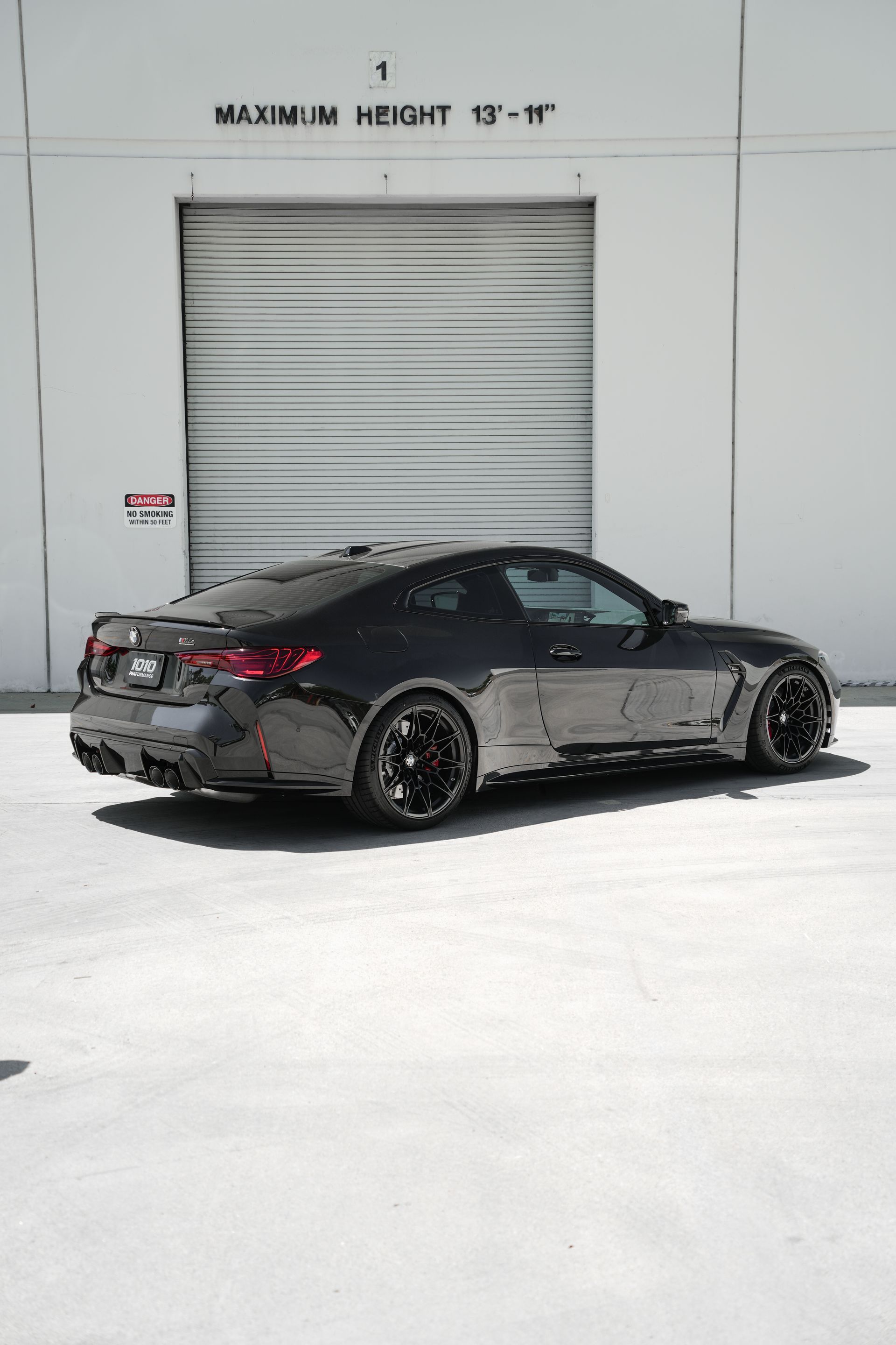 Black sports car parked in front of a white garage door on a bright day