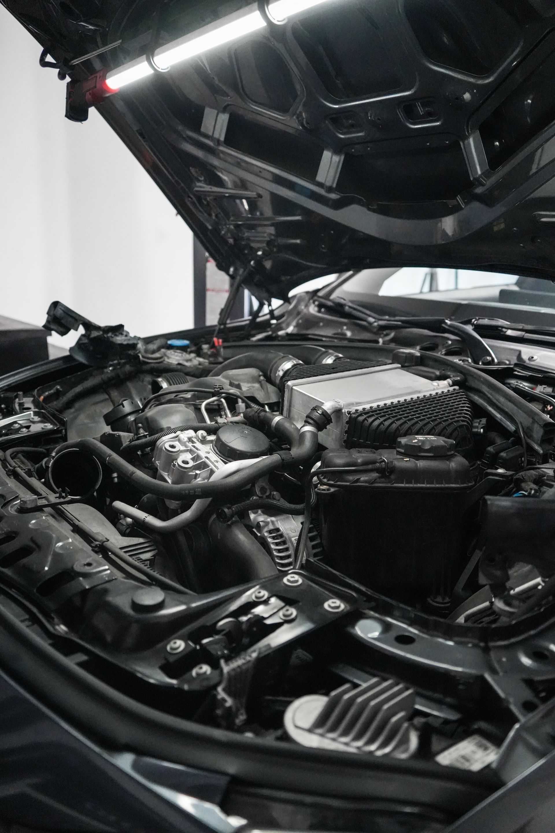 Car engine bay with hood open, showing shiny black components in a garage.
