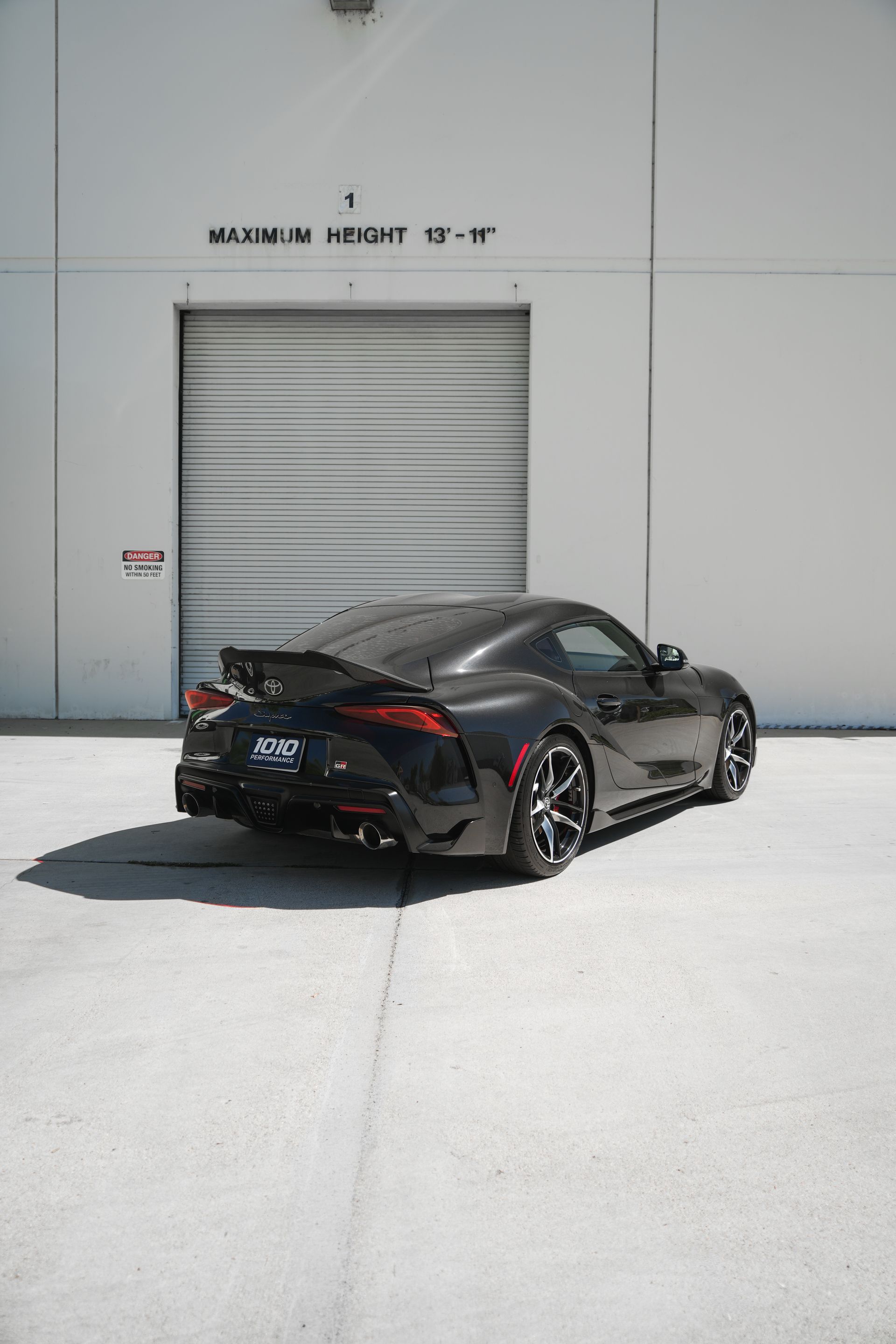 Black sports car parked outside a gray industrial building with a roll-up door