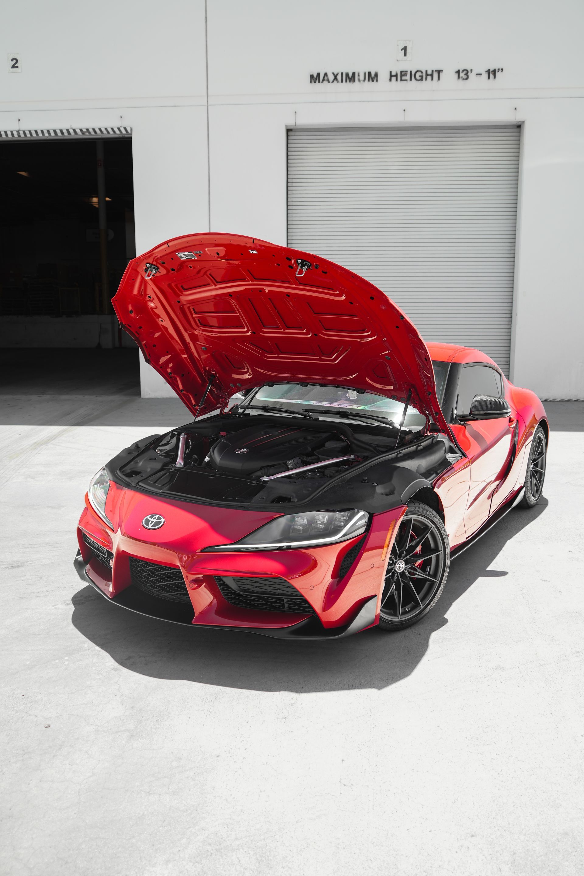 Red sports car with hood open in front of a garage door.